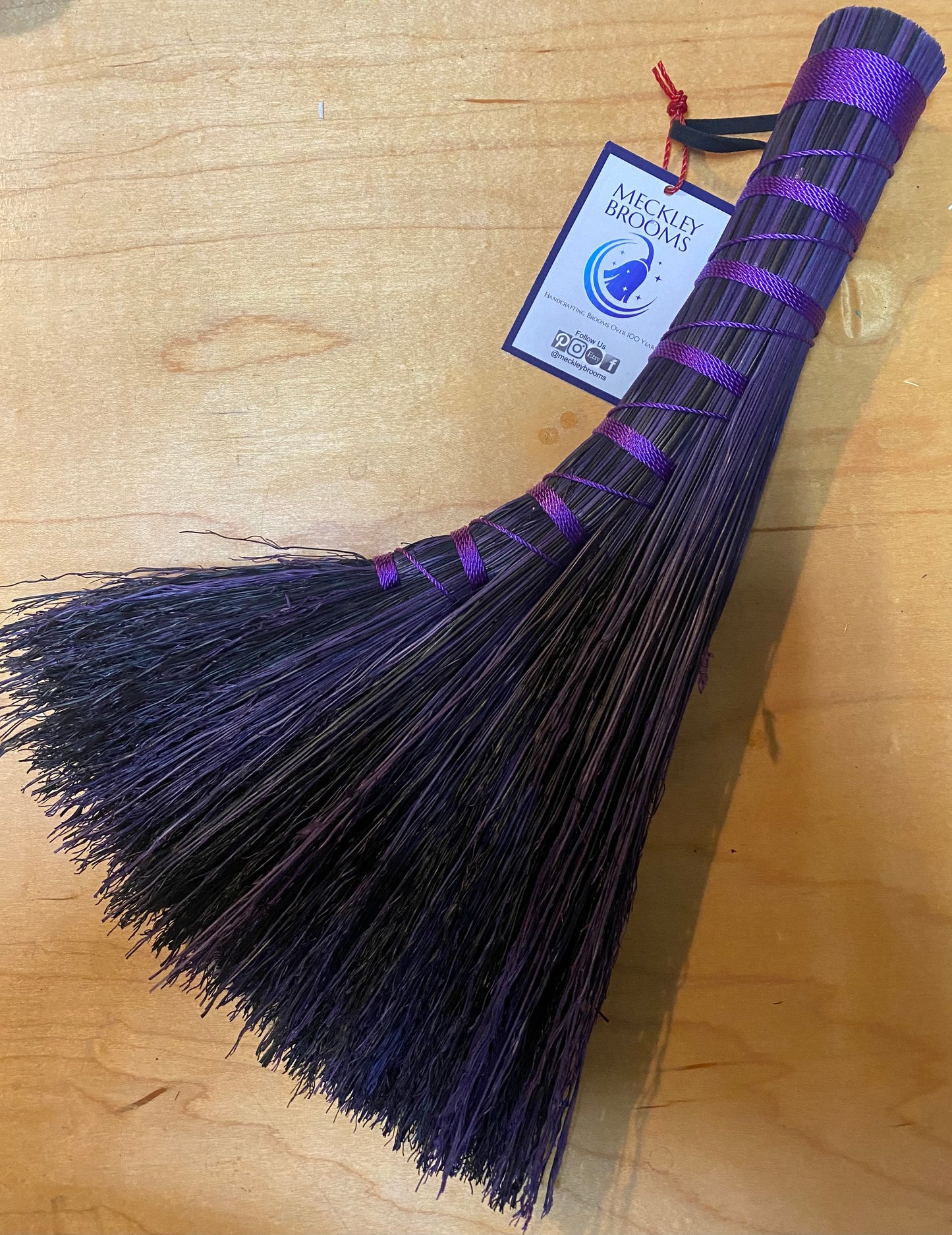Black broom with purple accents on a wooden surface, featuring a brand tag.