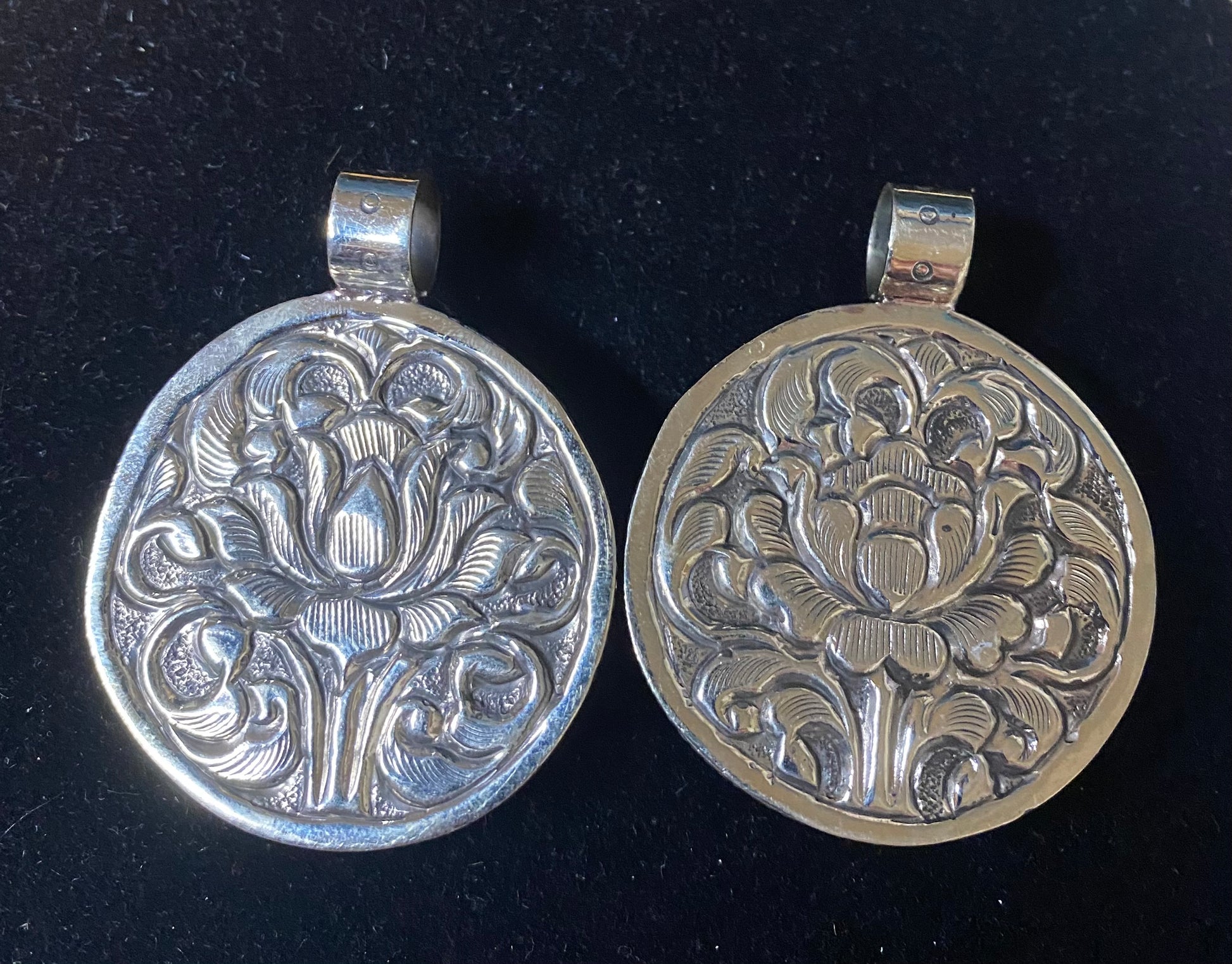 Two silver pendants with floral patterns on a black background