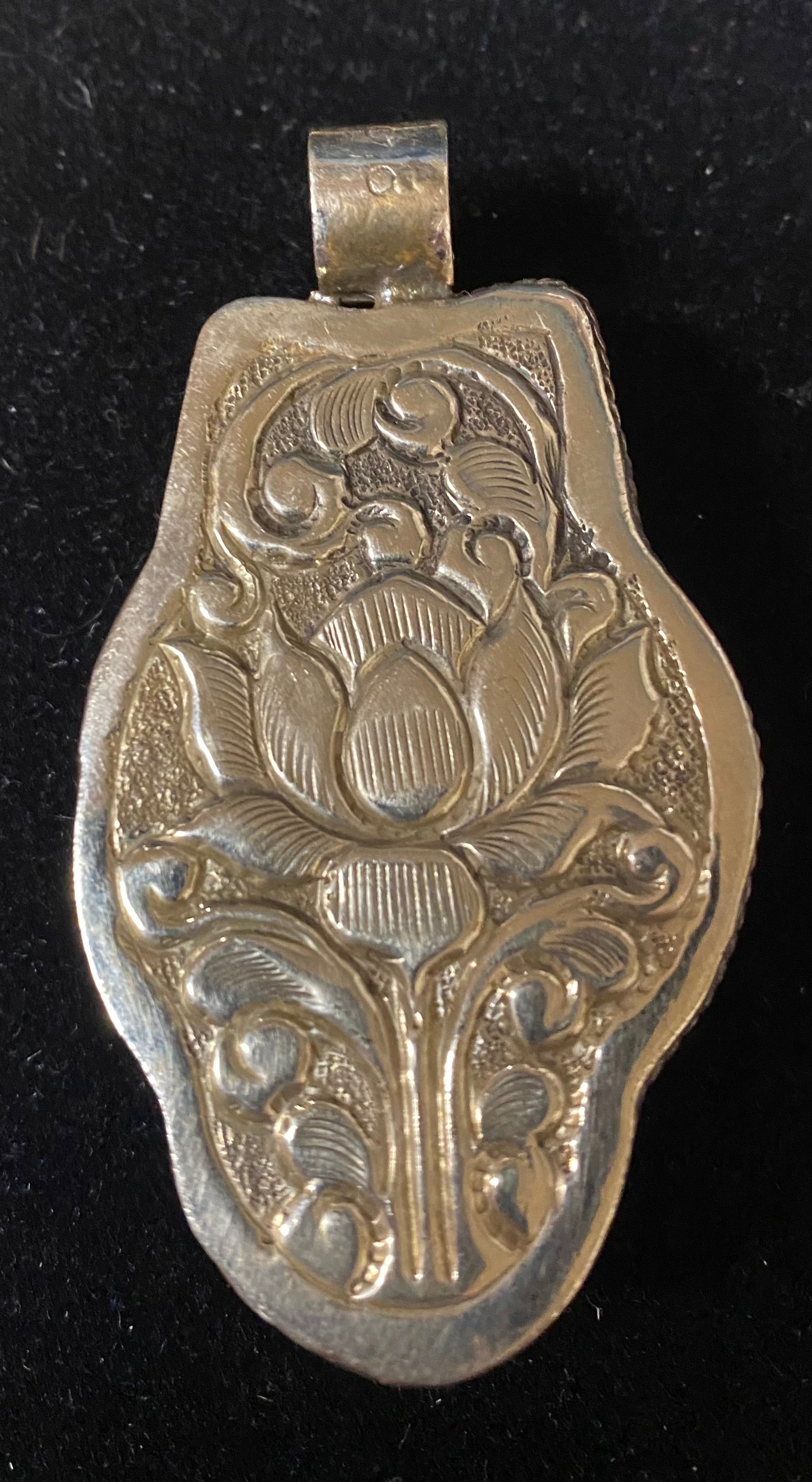 Silver pendant with intricate design on a black background