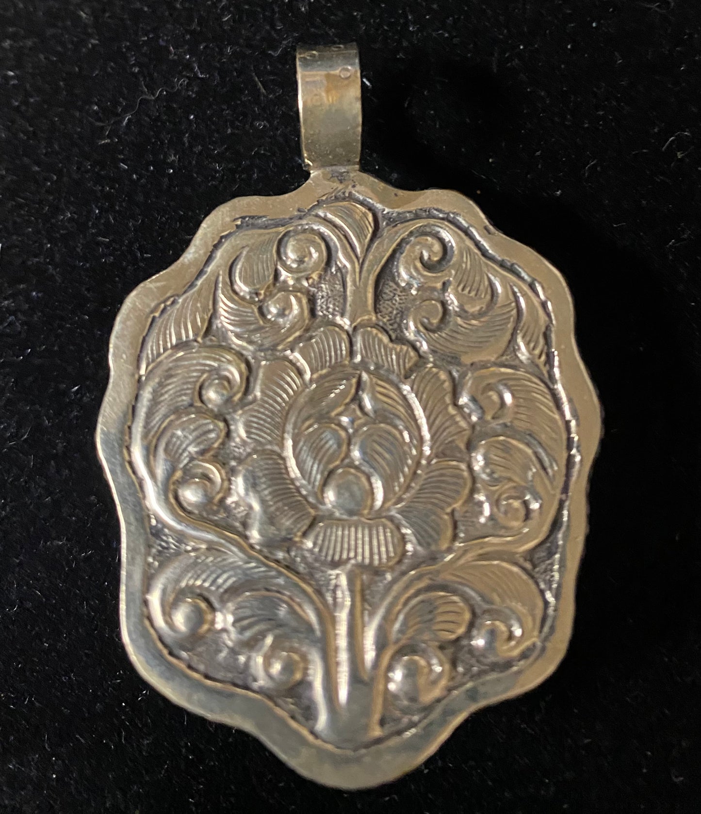 Silver pendant with intricate floral design on a black background