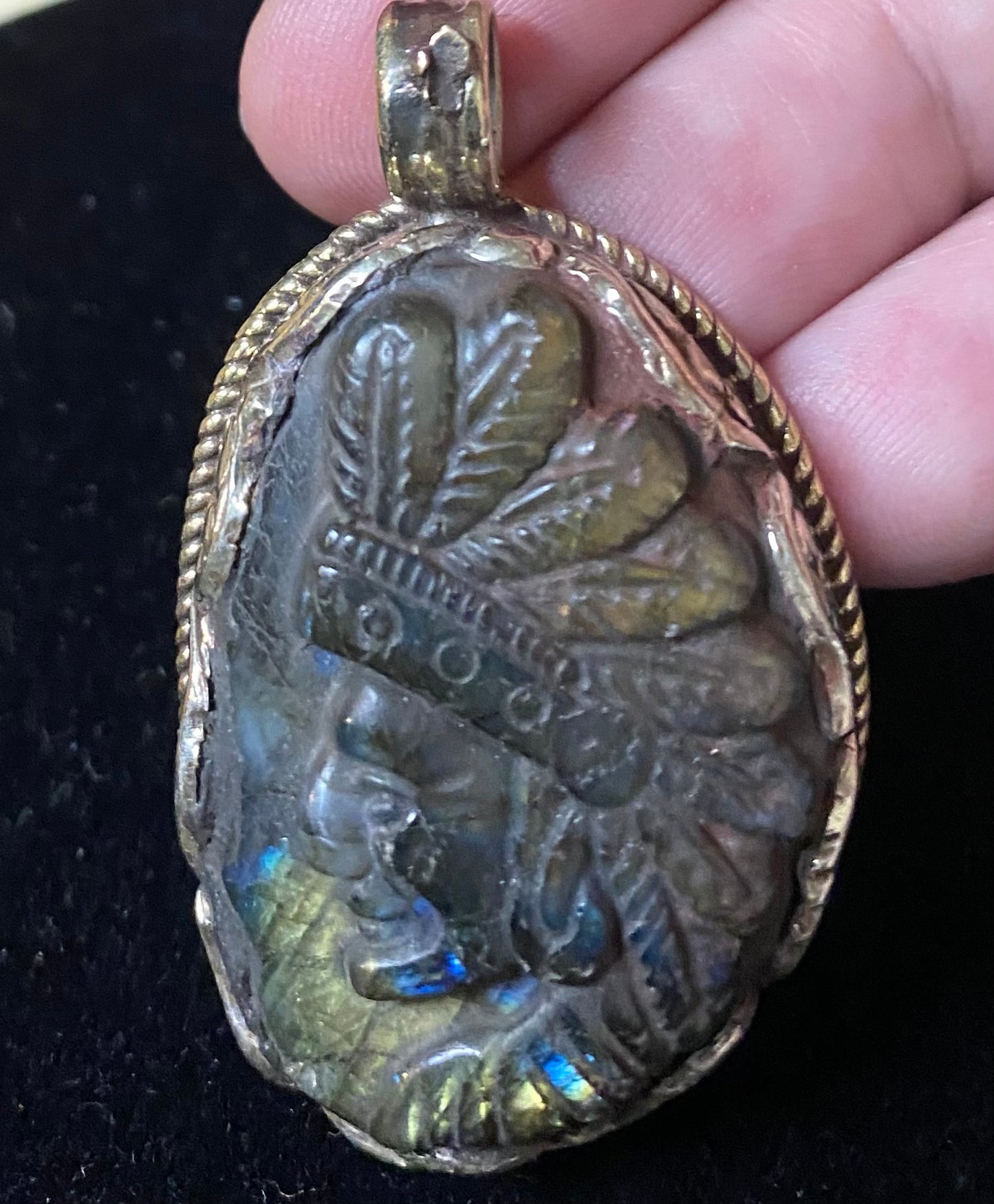 Decorative pendant with intricate design held by a hand on a dark background