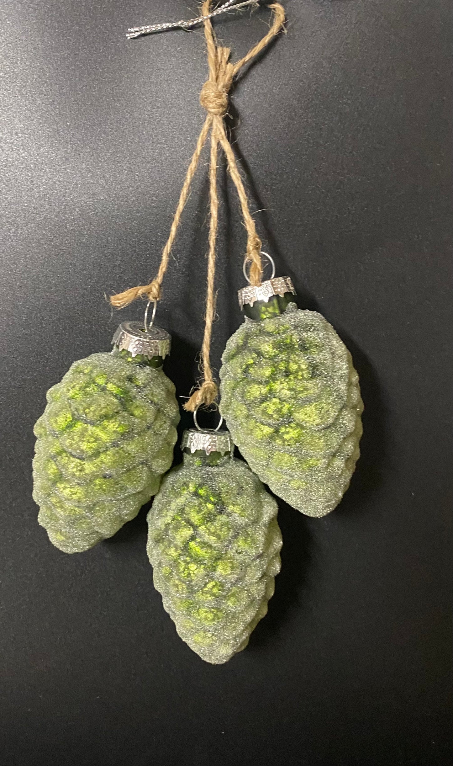 Green pine cone-shaped ornaments hanging on a black background