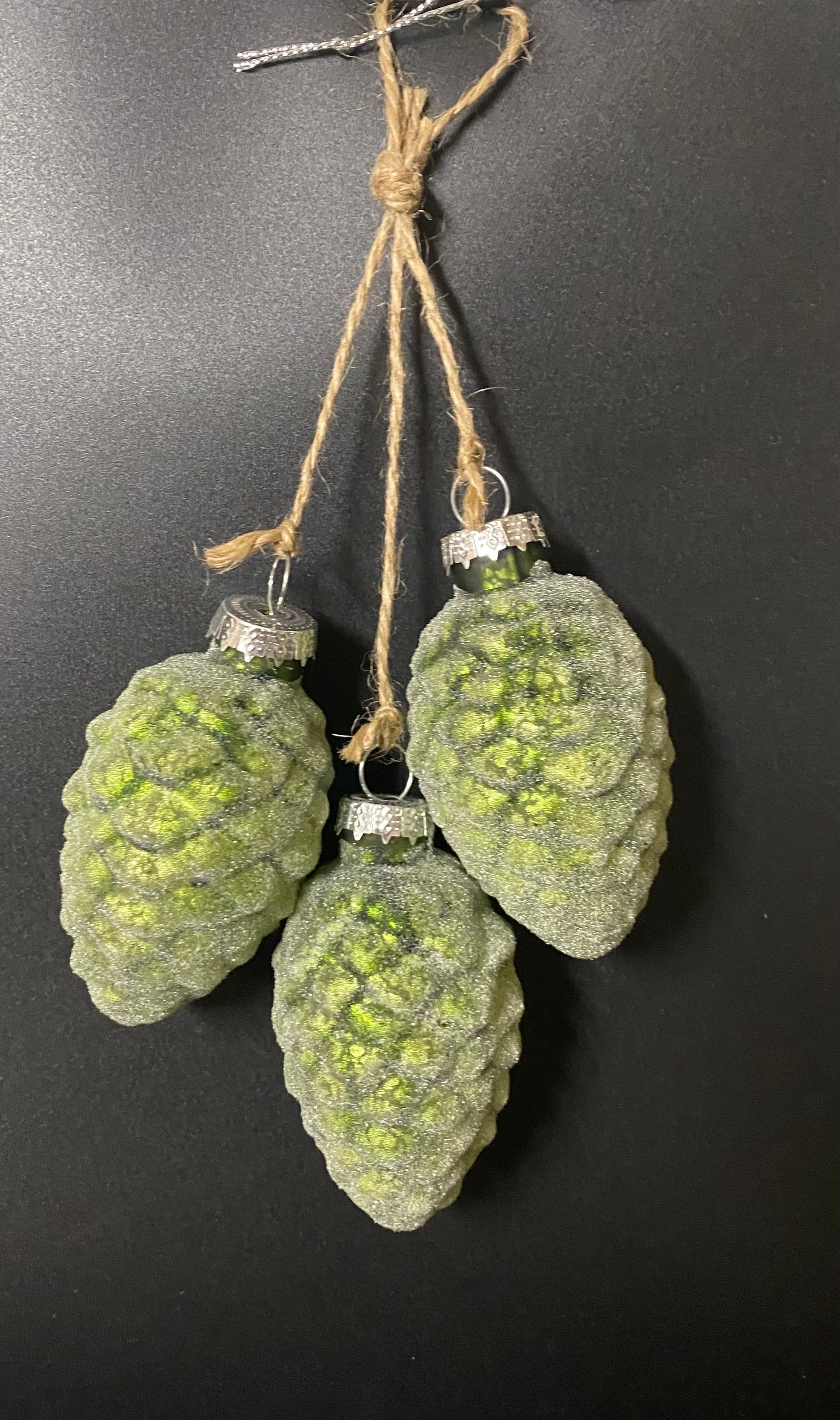 Green pine cone-shaped ornaments hanging on a black background