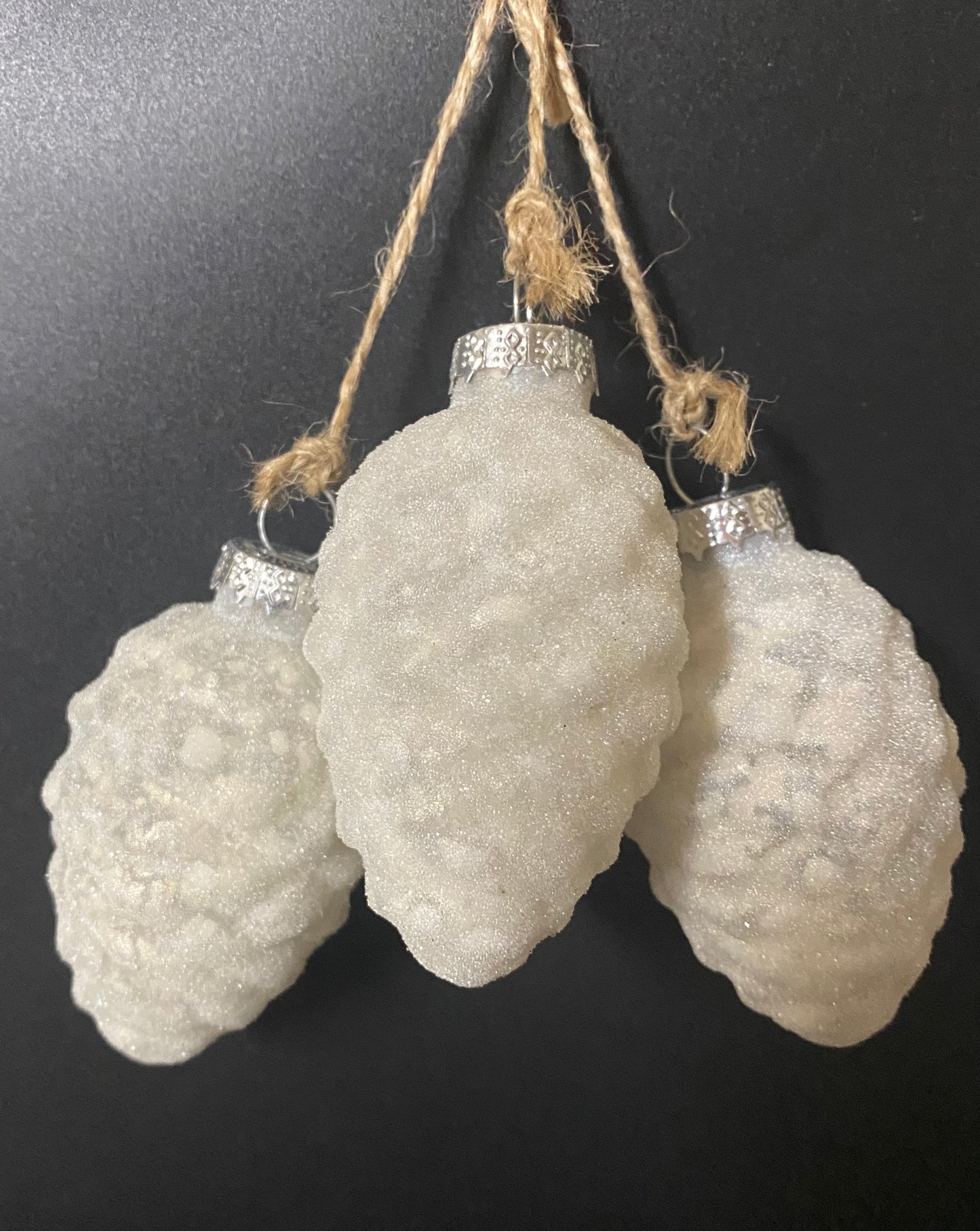 Three textured white ornaments with silver bases hanging on a black background