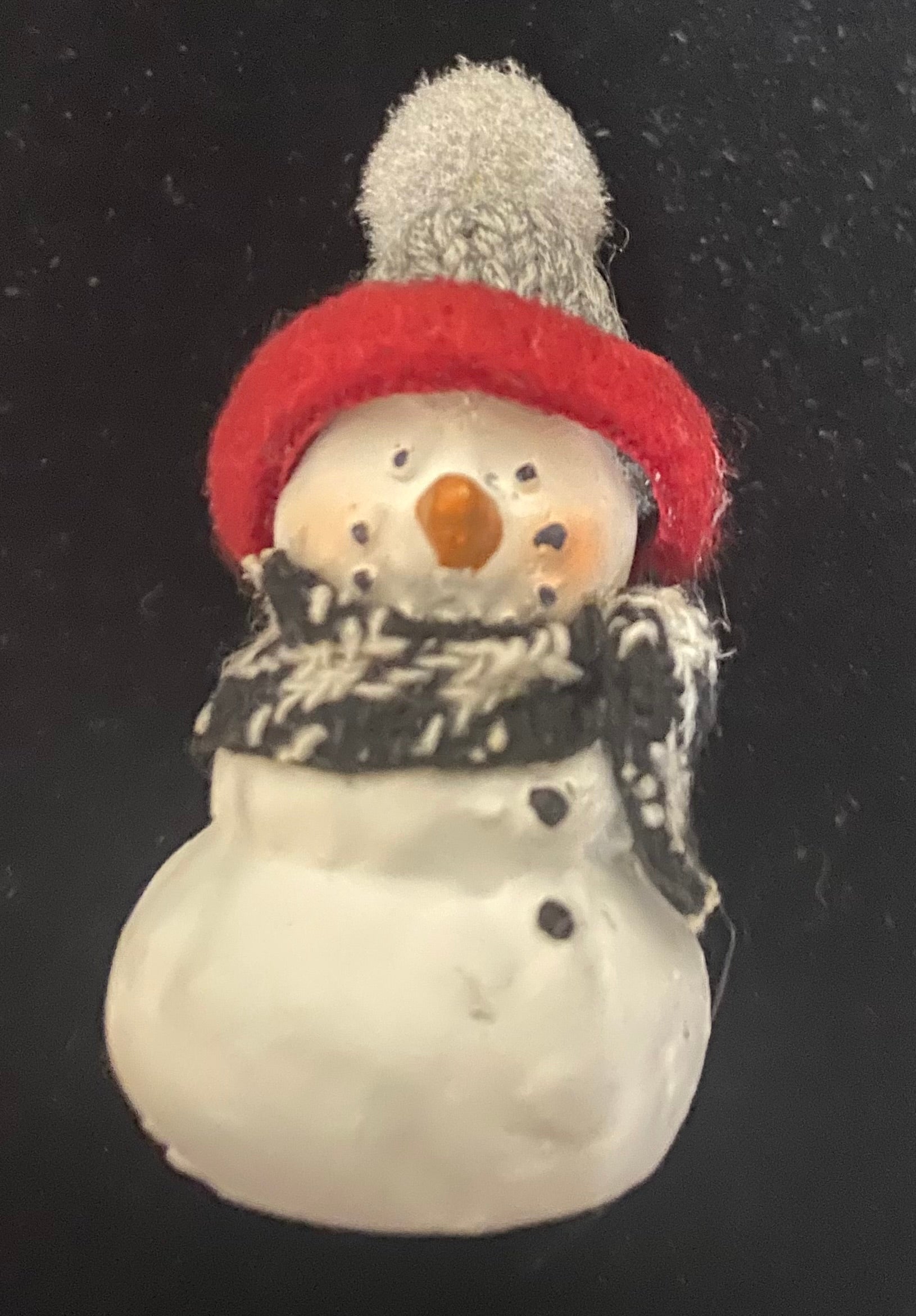 Small snowman figurine with a red hat and black scarf on a dark background