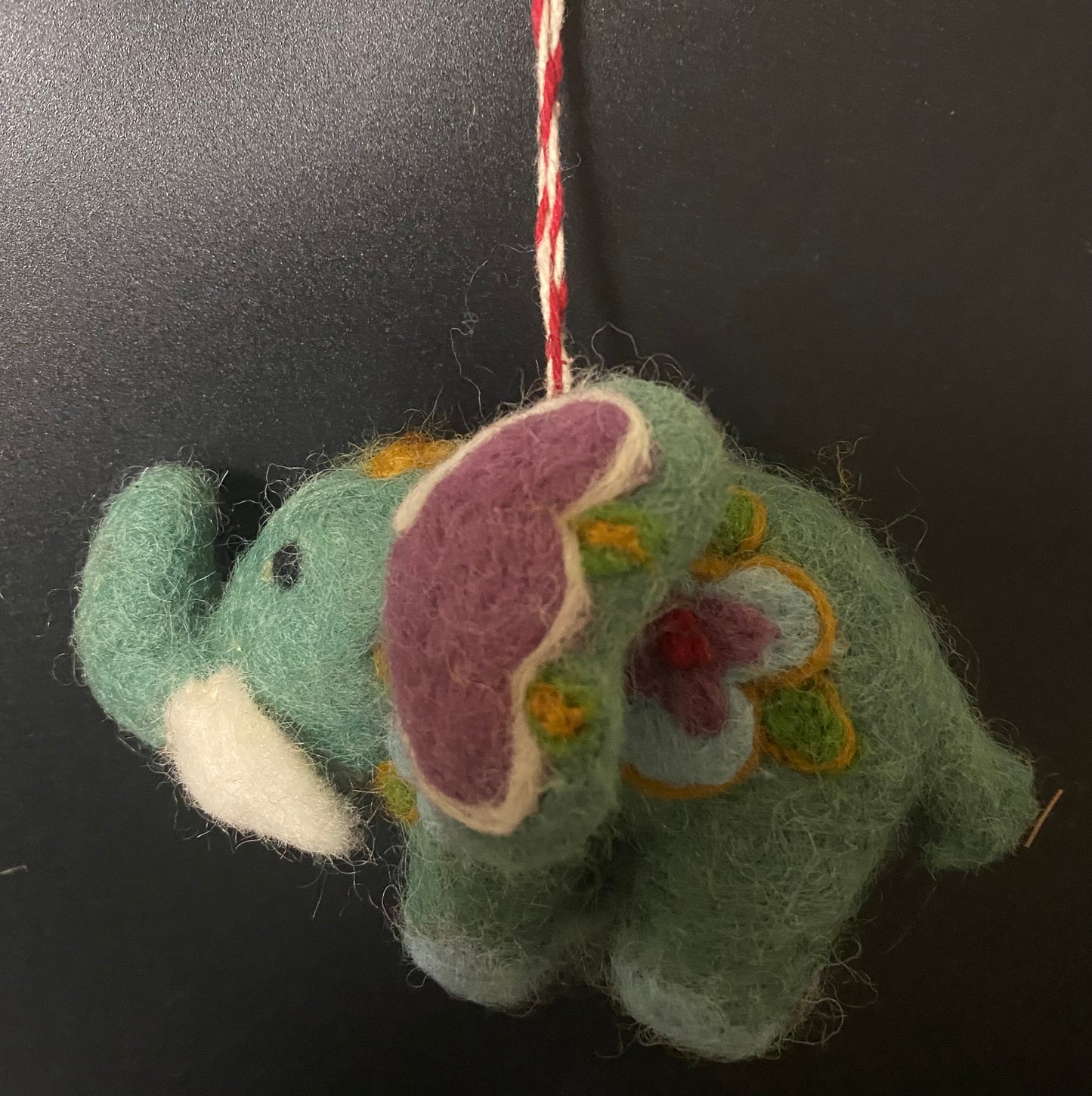Handmade felted green elephant ornament with floral patterns on a black background