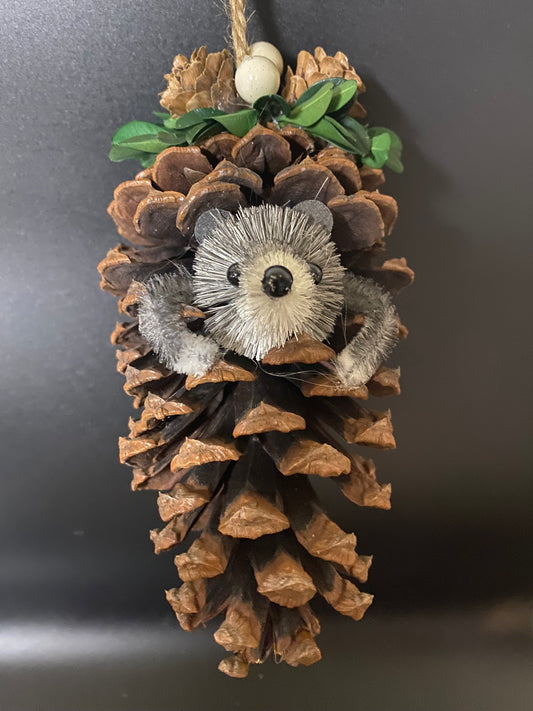 Decorative item with pine cones, green leaves, and a white flower-like object on a dark background