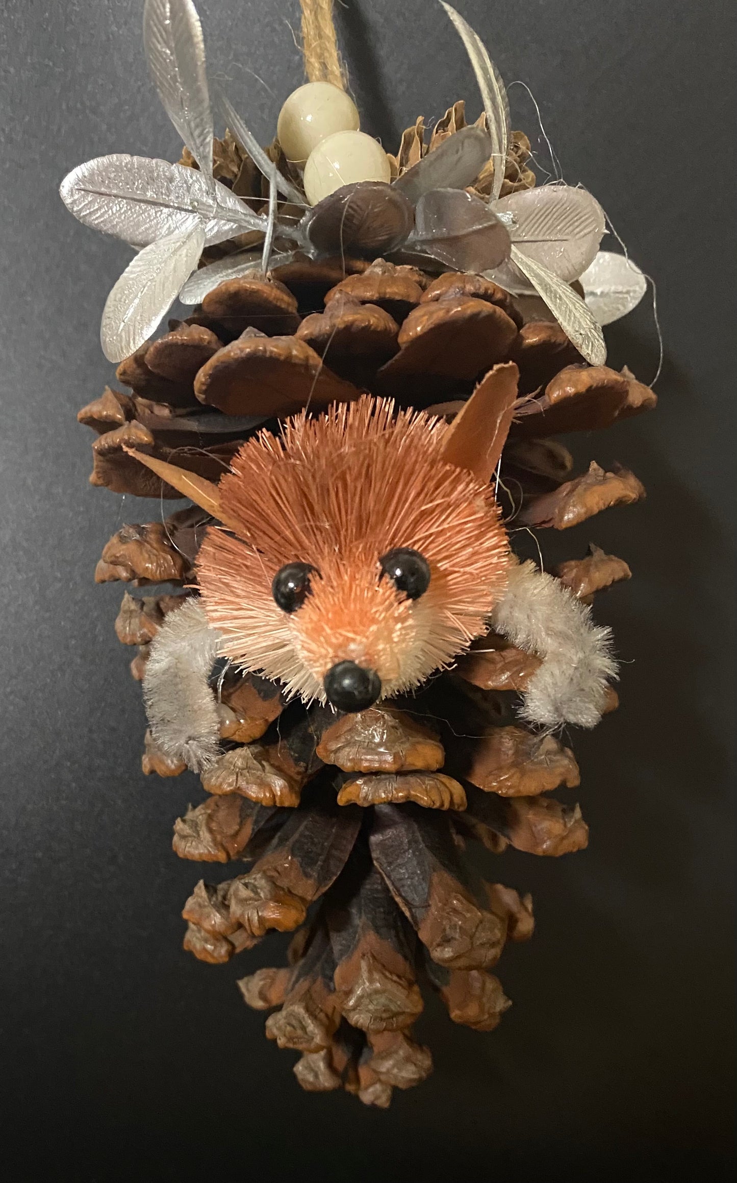 Decorative fox ornament made from pinecones and feathers on a dark background