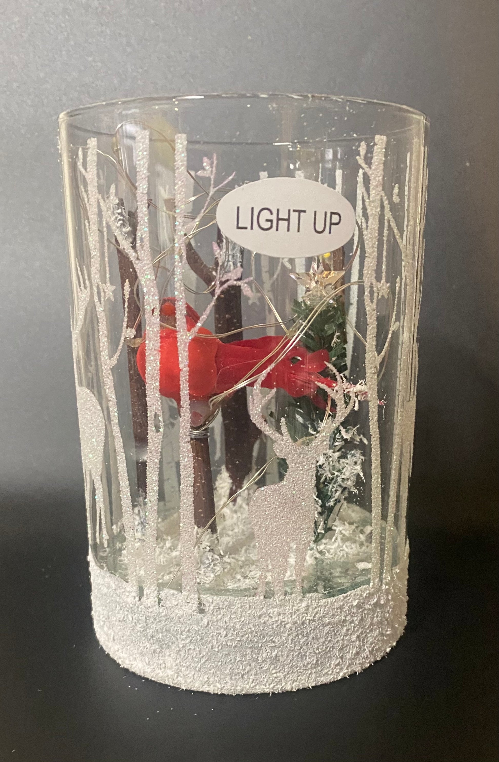 Decorative glass with winter scene and 'Light Up' label on a dark background
