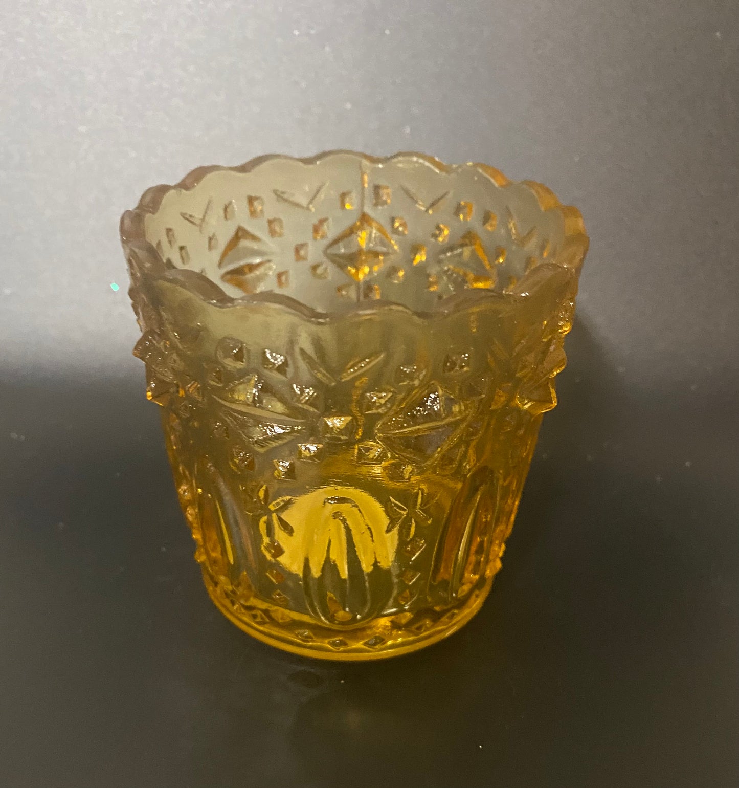 Decorative yellow glass candle holder with intricate patterns on a dark background