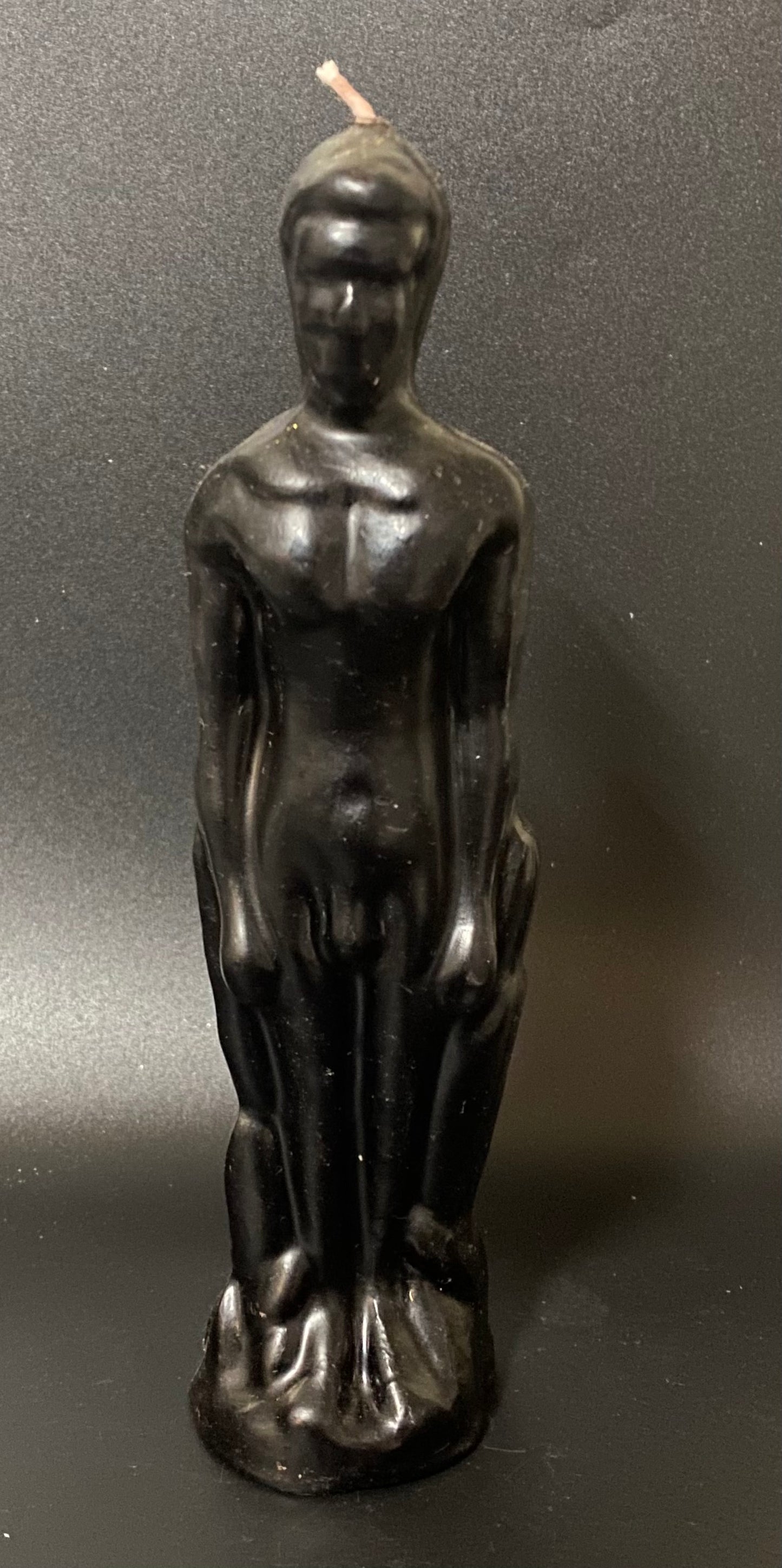Black candle shaped like a nude figure on a dark background