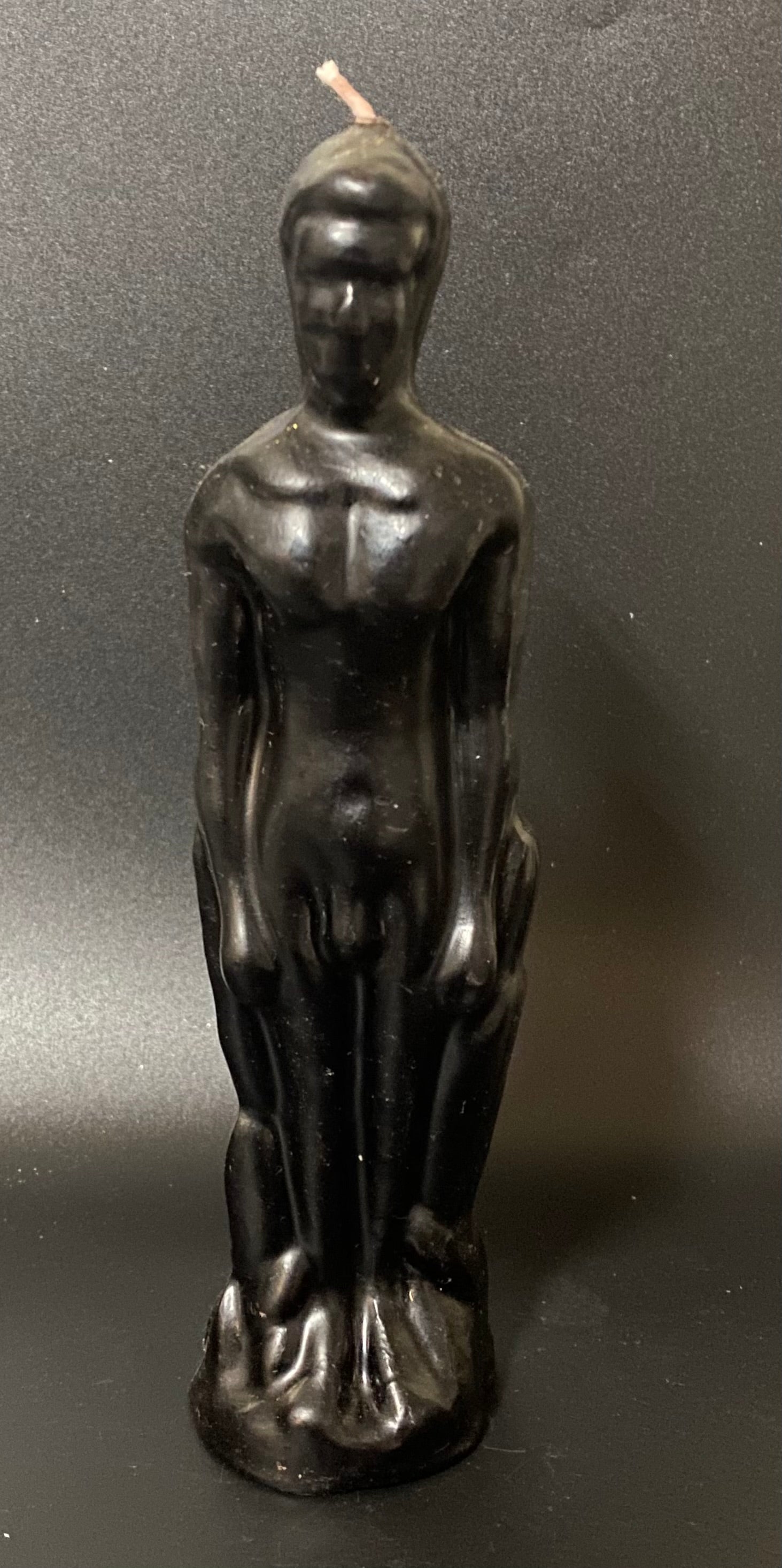 Black candle shaped like a nude figure on a dark background