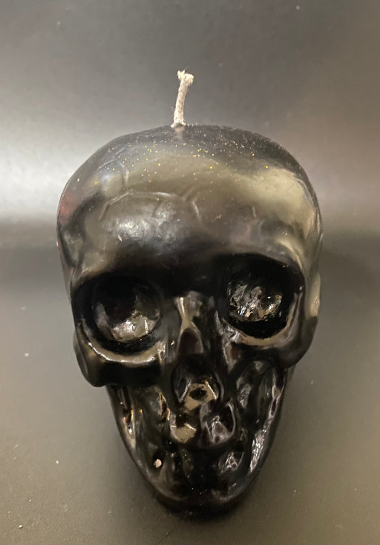 Black skull-shaped candle on a reflective surface