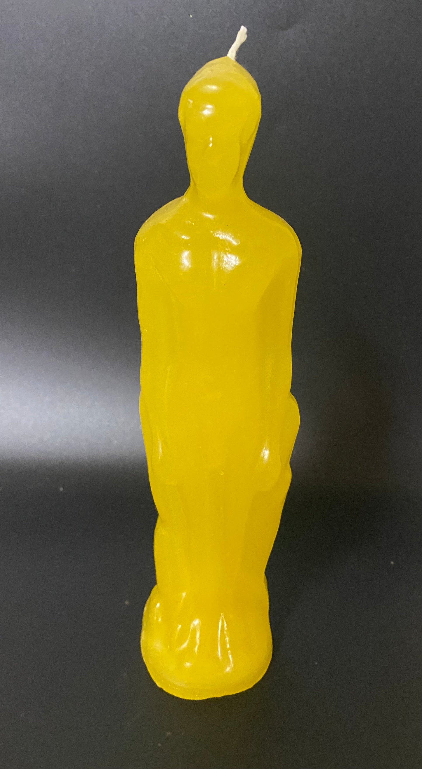 Yellow candle shaped like a person on a black background