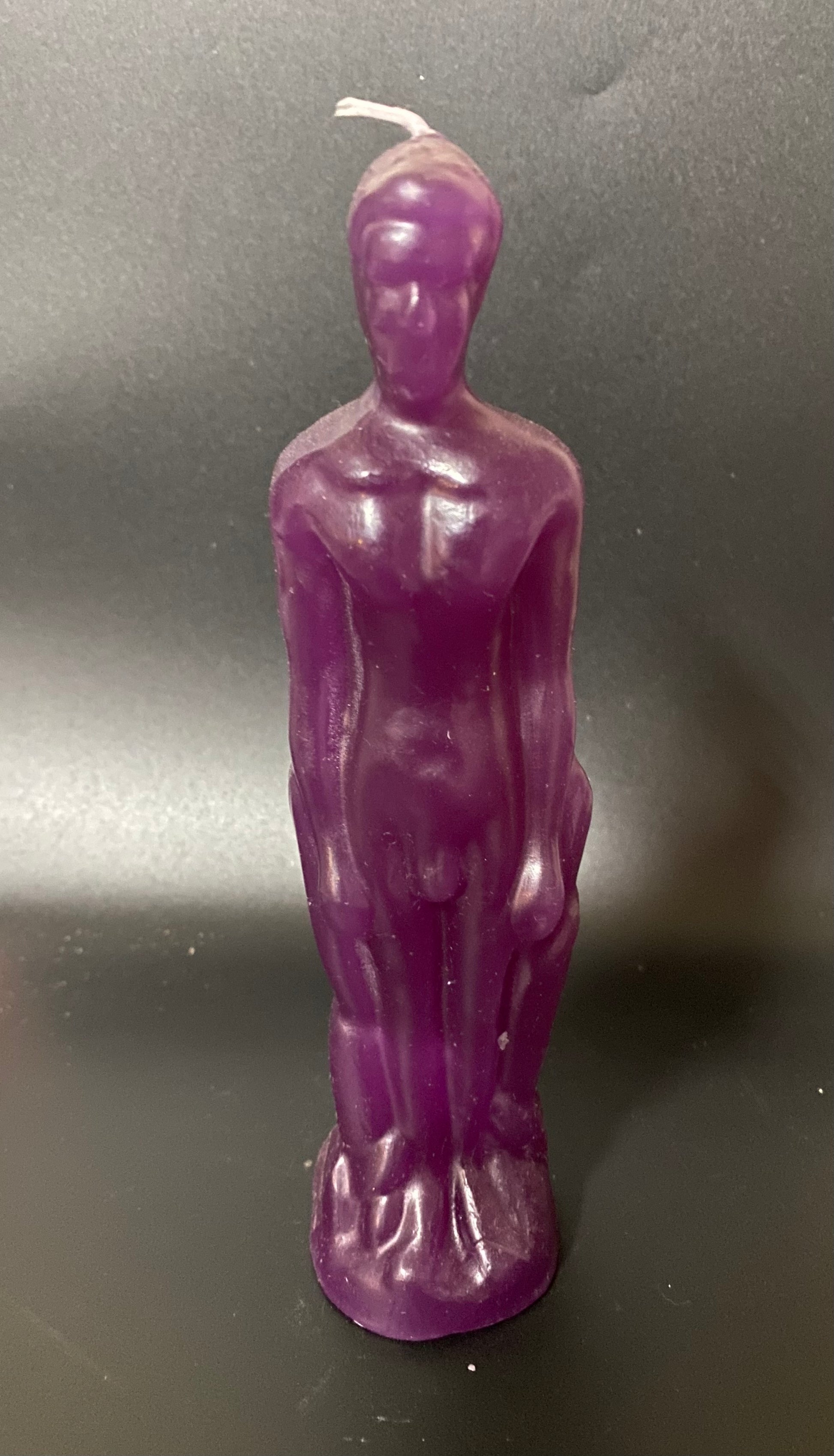 Purple candle shaped like a standing figure on a dark background