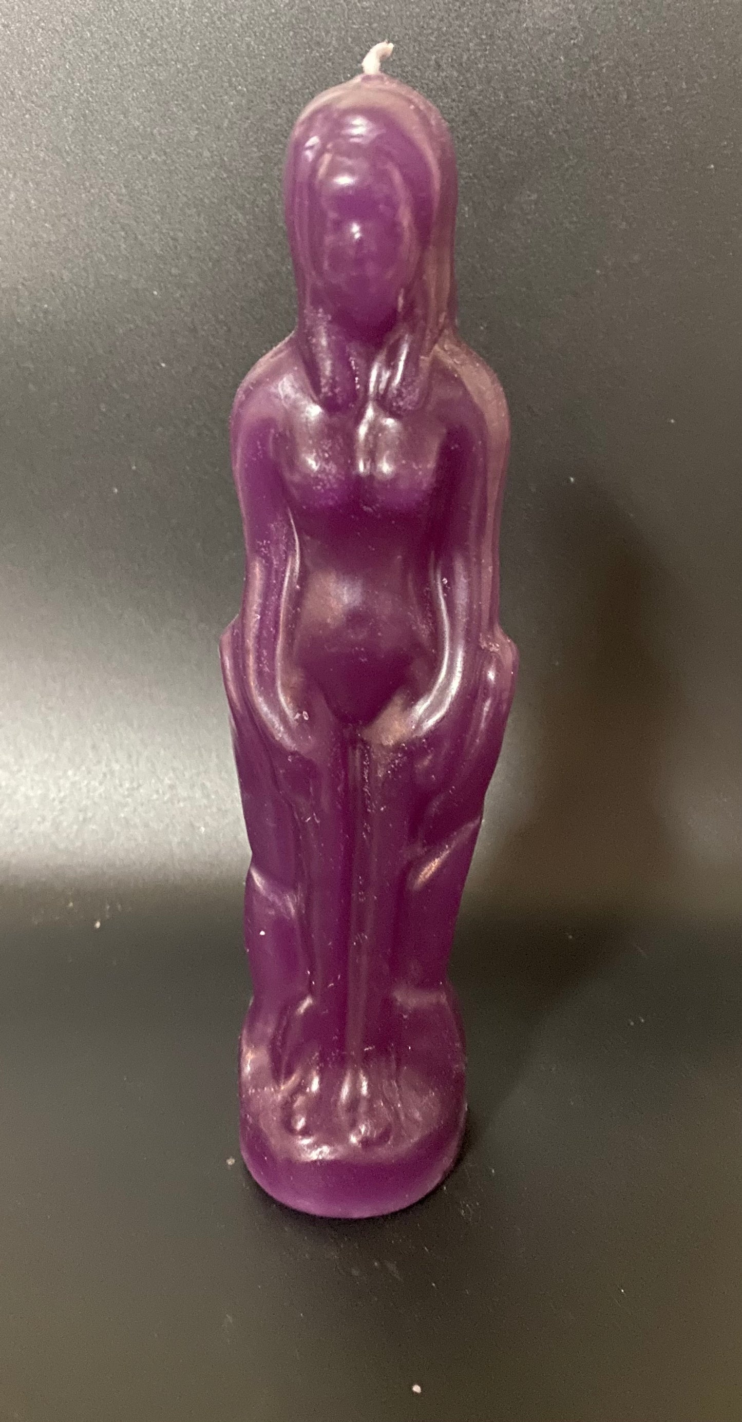 Purple candle shaped like a human figure on a dark background