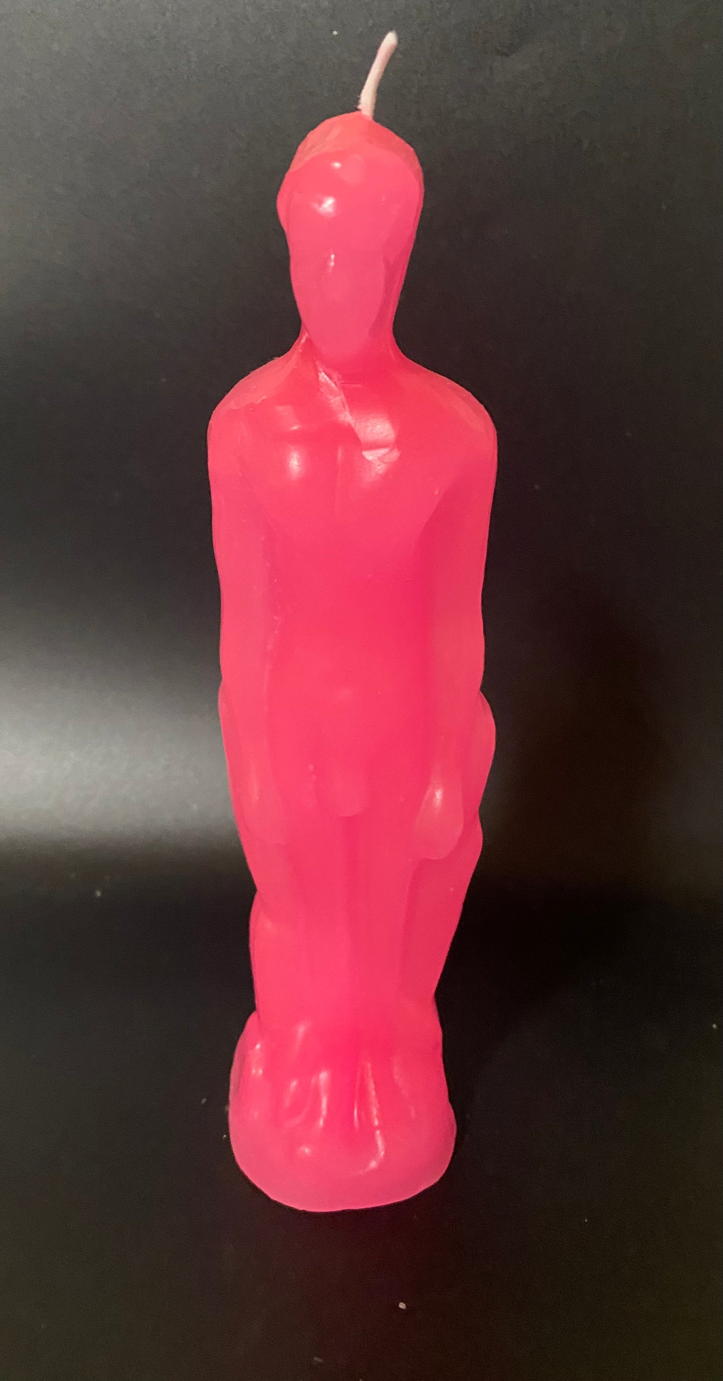 Pink candle shaped like a person on a black background