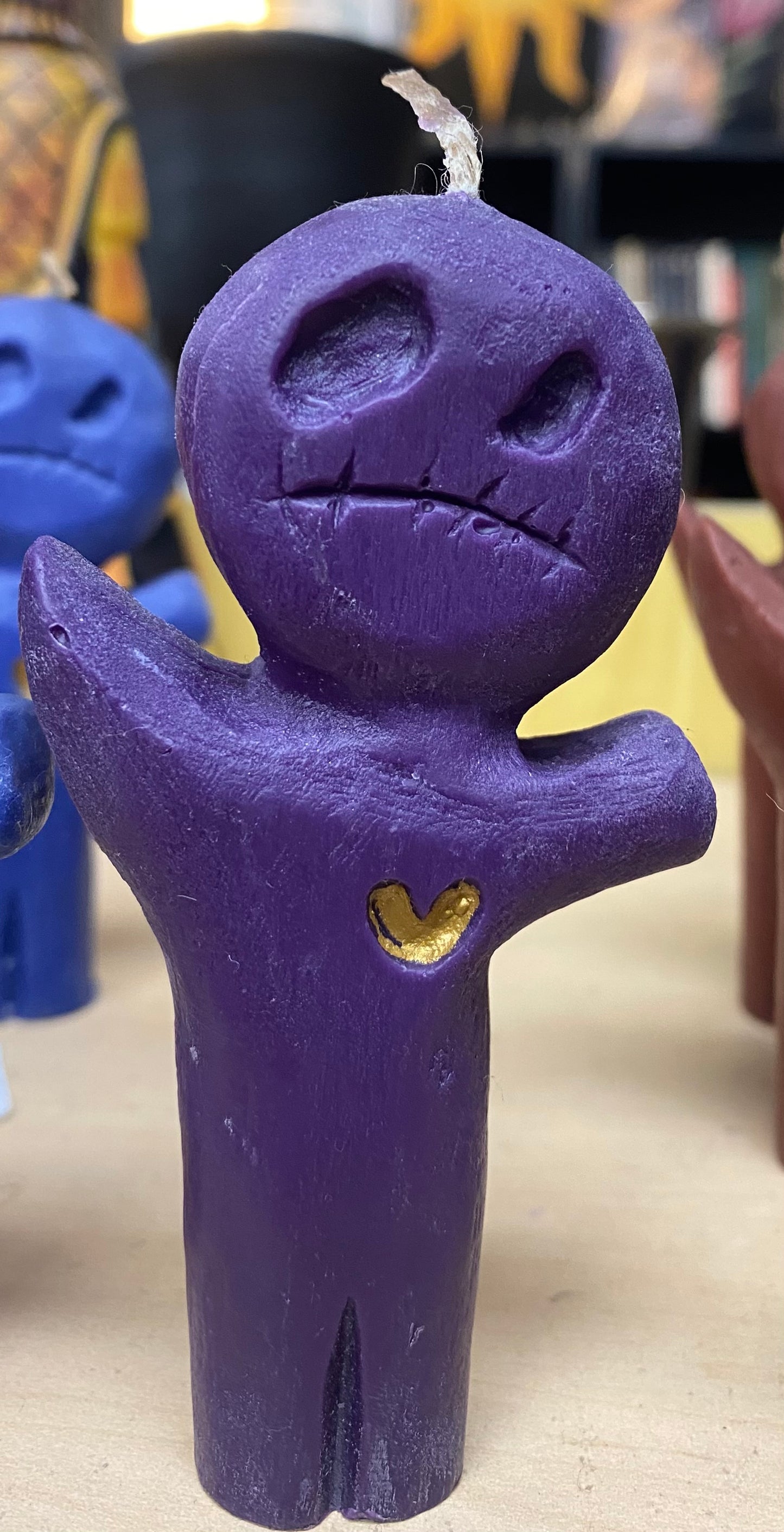 Purple candle figurine with a gold heart on a neutral background