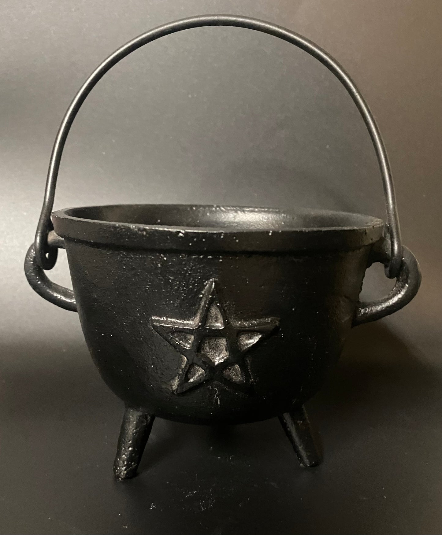 Black cast iron cauldron with a pentagram design on a dark background
