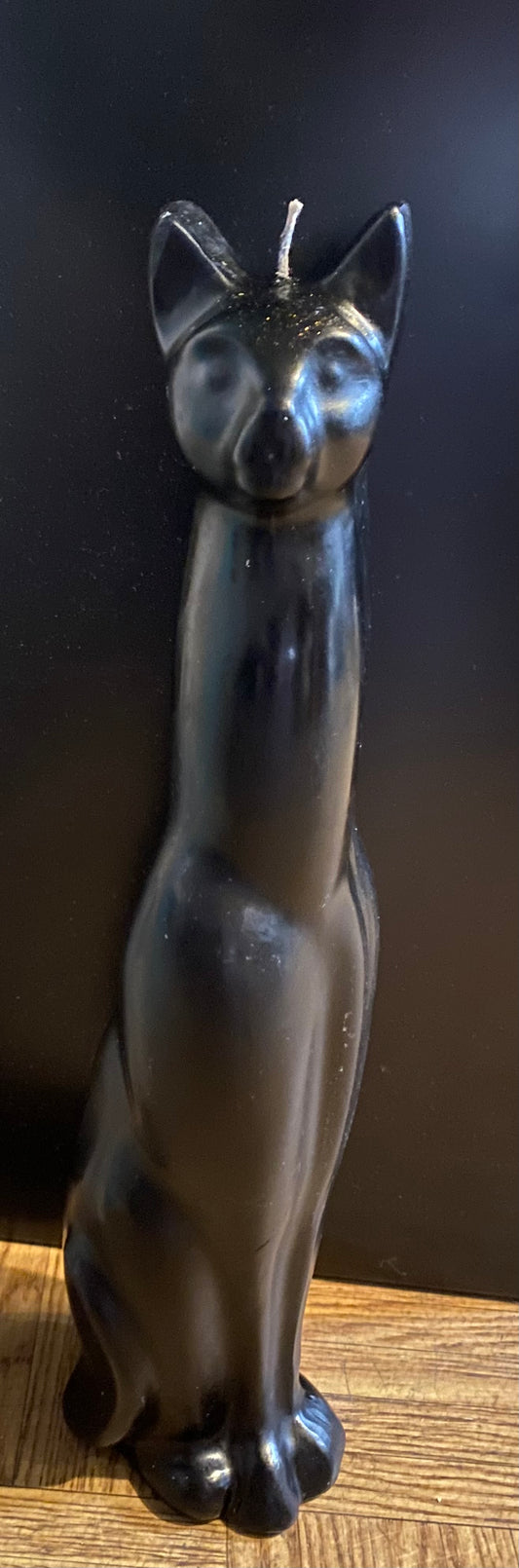 Black cat-shaped candle on a wooden surface with a dark background