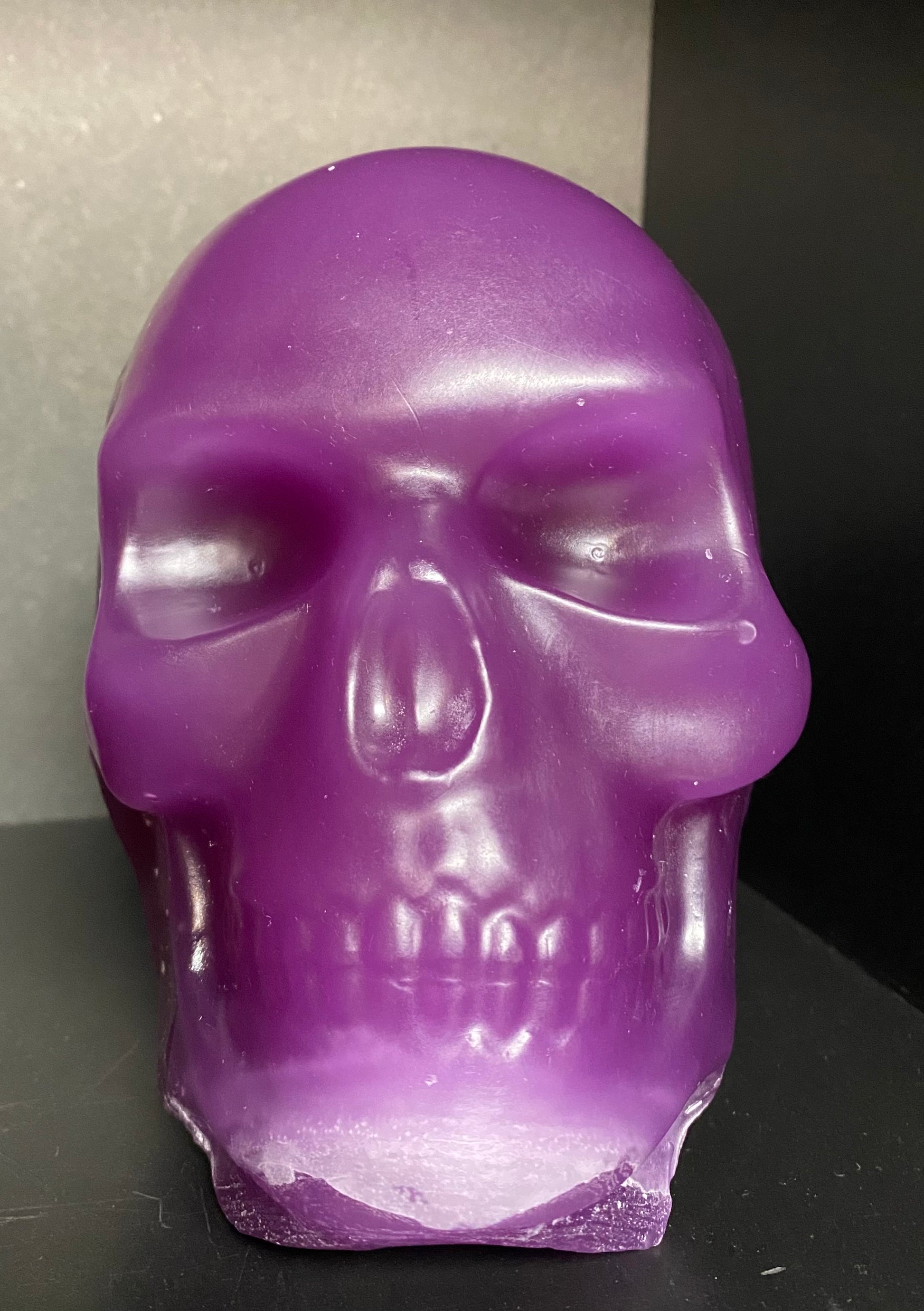 Purple skull-shaped candle on a dark surface with a neutral background