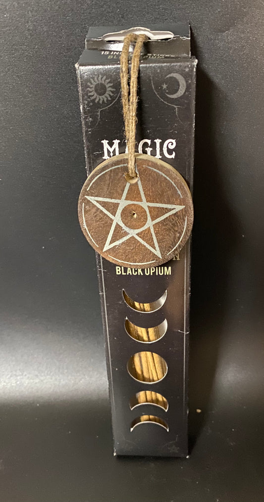Wooden pentacle charm on a black box labeled 'Magic Black Opium' against a dark background