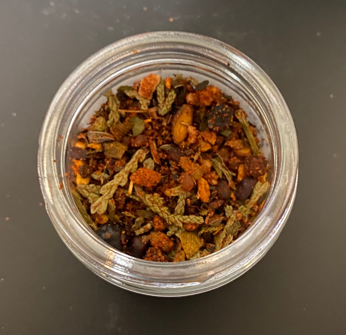 Clear glass jar filled with dried herbs and spices on a dark background