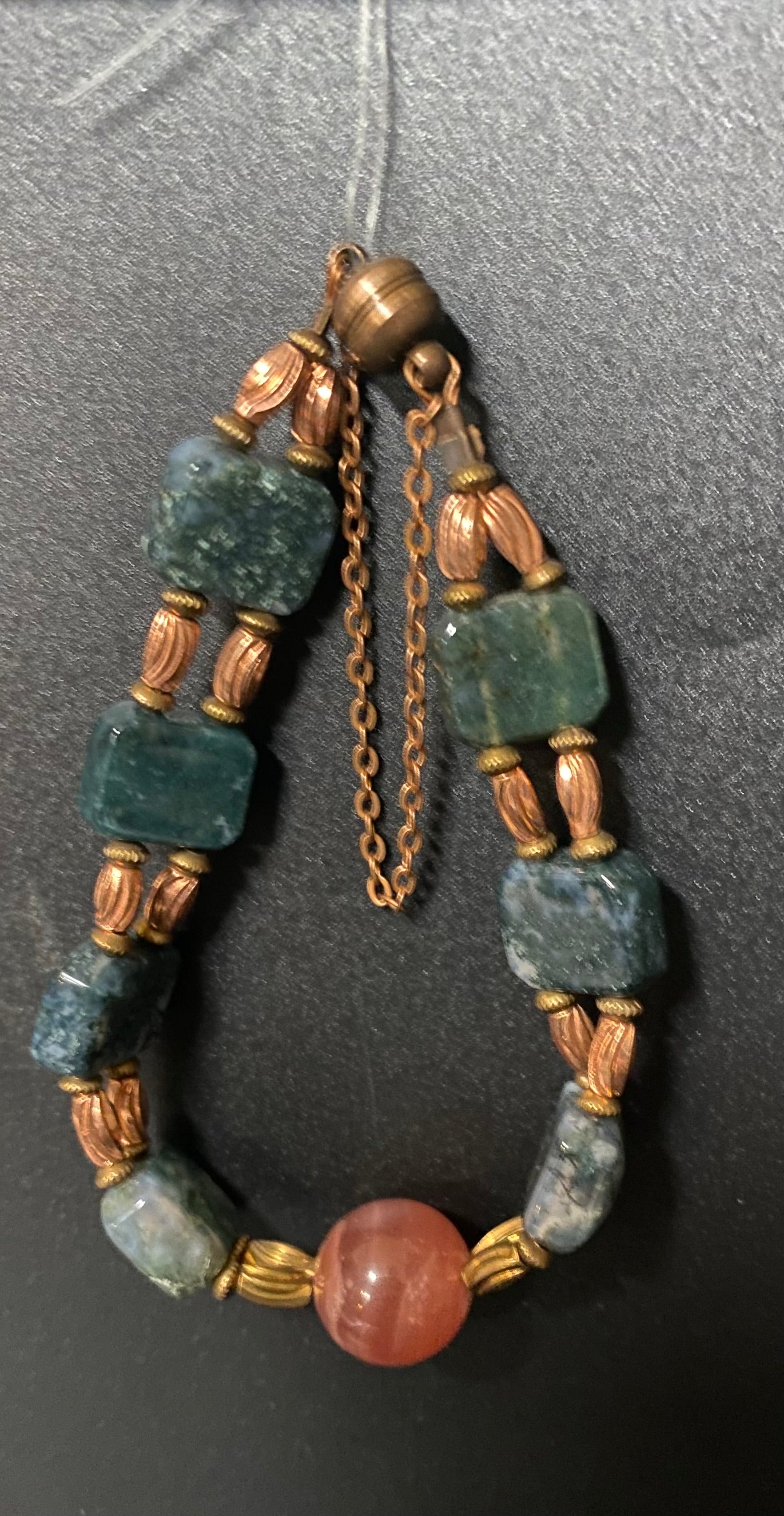 Bracelet with green beads and a pink stone on a dark background