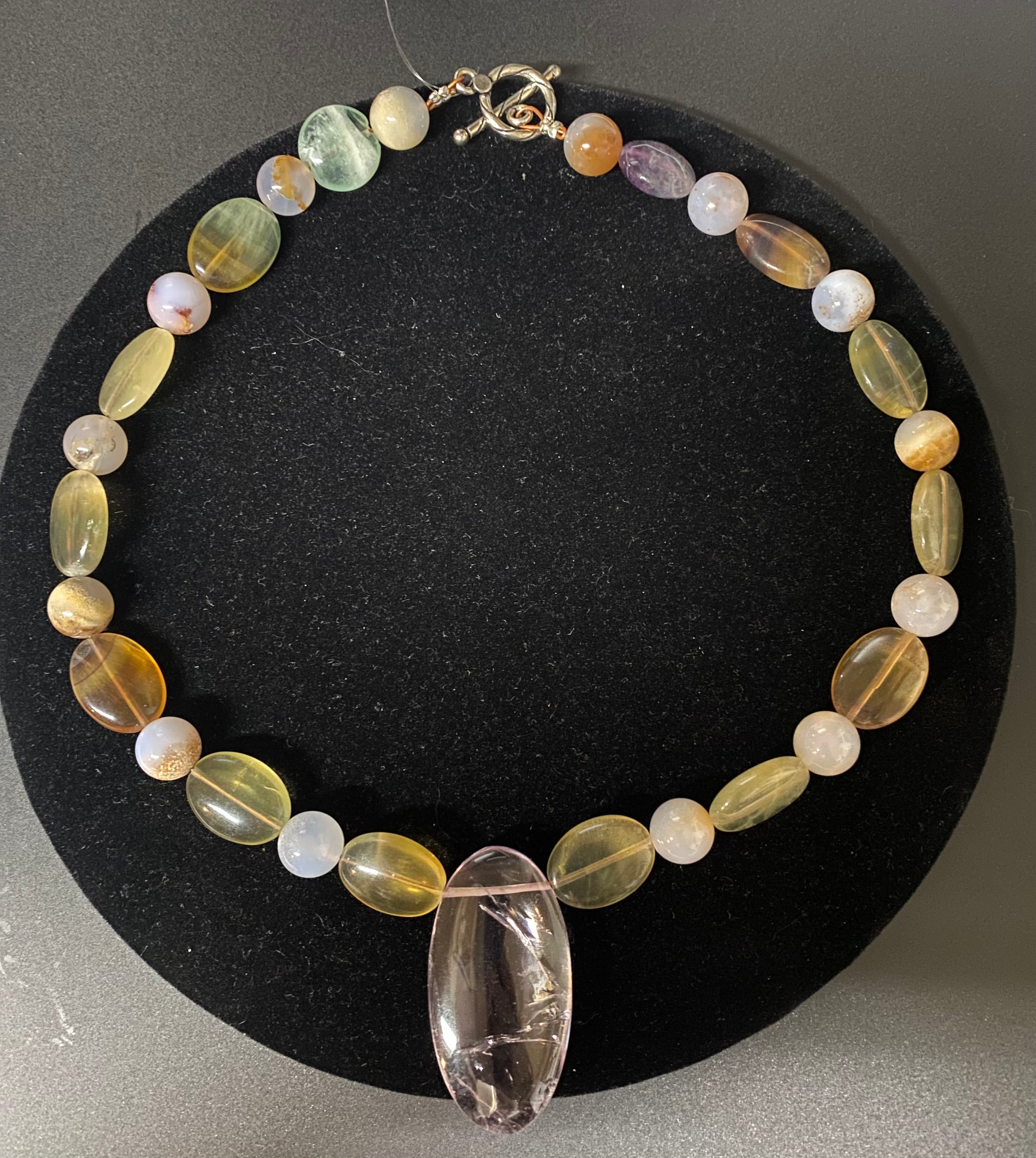 Necklace with multicolored beads and a clear crystal pendant on a black background