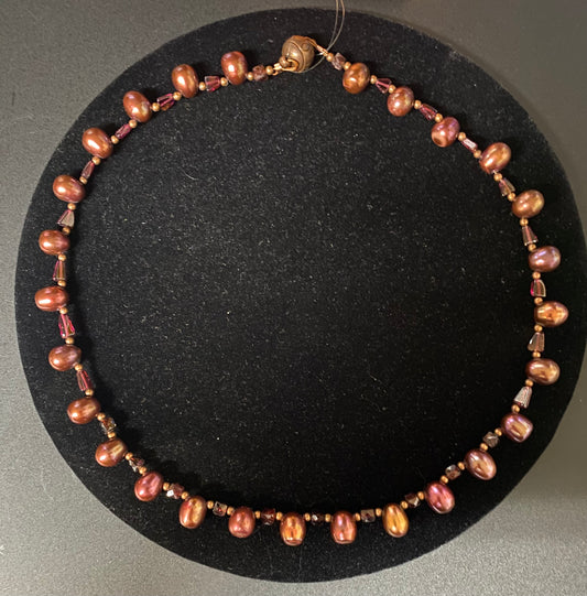 Necklace with brown and pink beads on a black circular stand