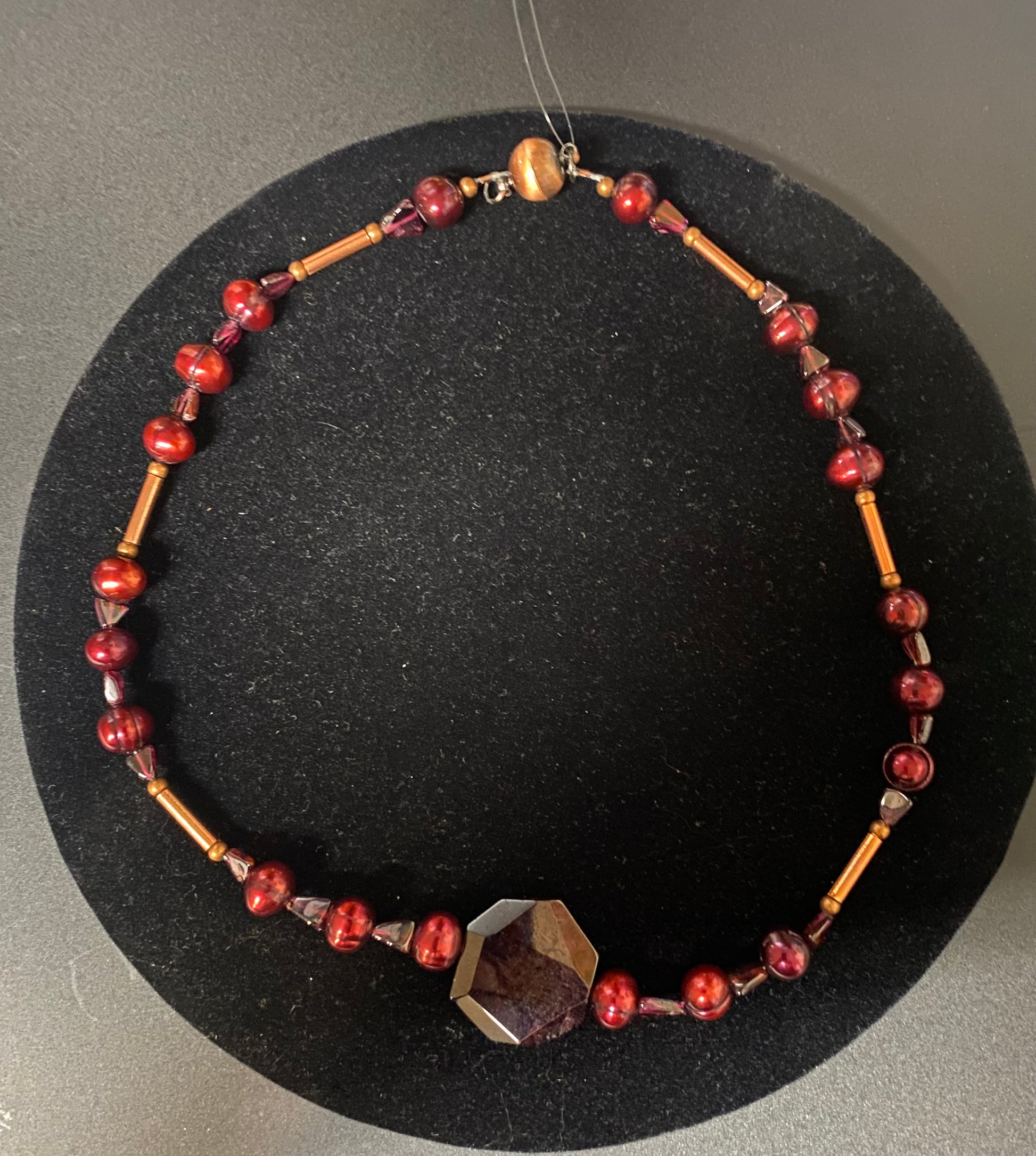 Necklace with red and gold beads on a black stand
