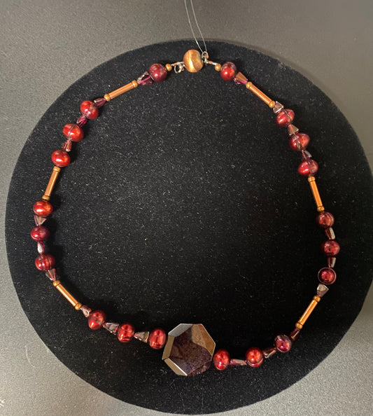 Necklace with red and gold beads on a black stand