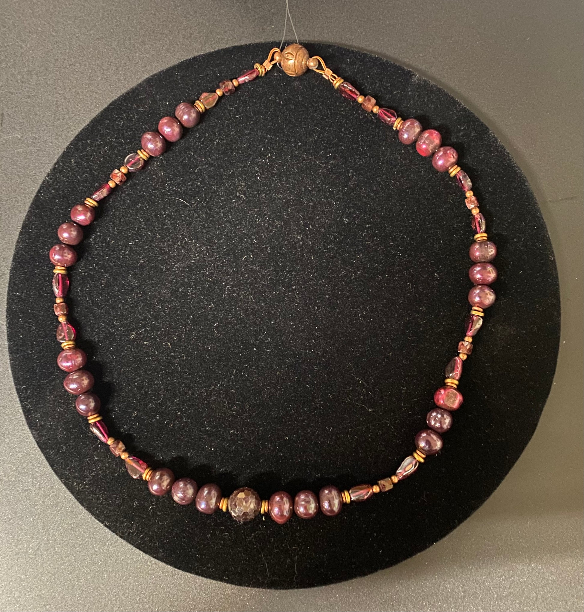 Necklace with pink beads and gold accents on a black stand