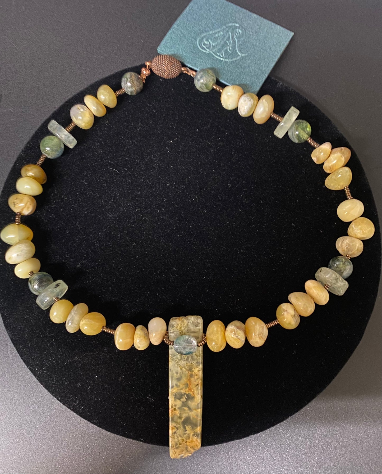 Necklace with beaded design and pendant on a black stand