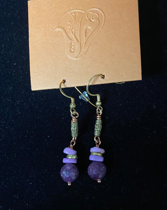 Pair of purple beaded earrings on a dark background with a brand card.