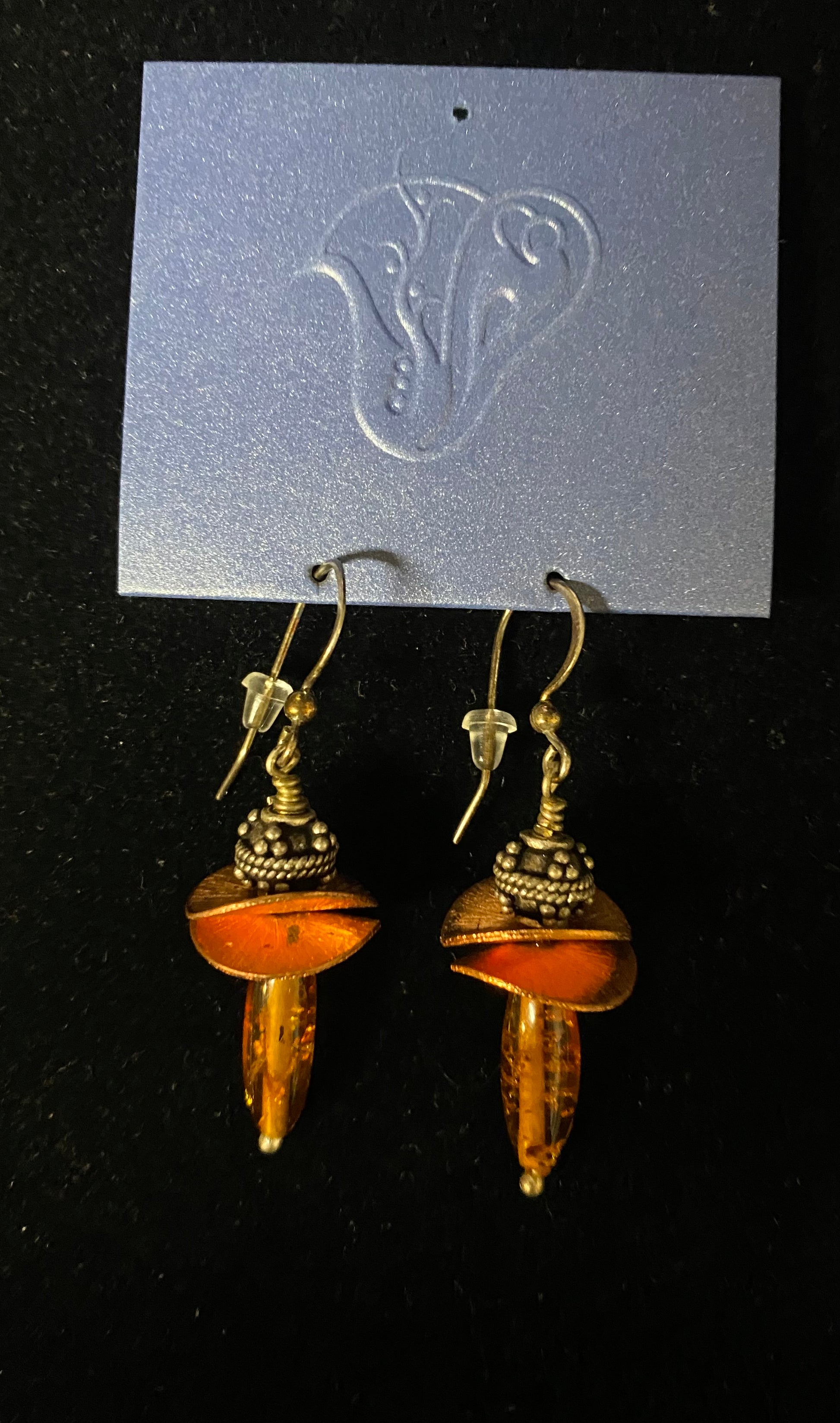 Pair of amber-colored earrings on a black background with a brand card.