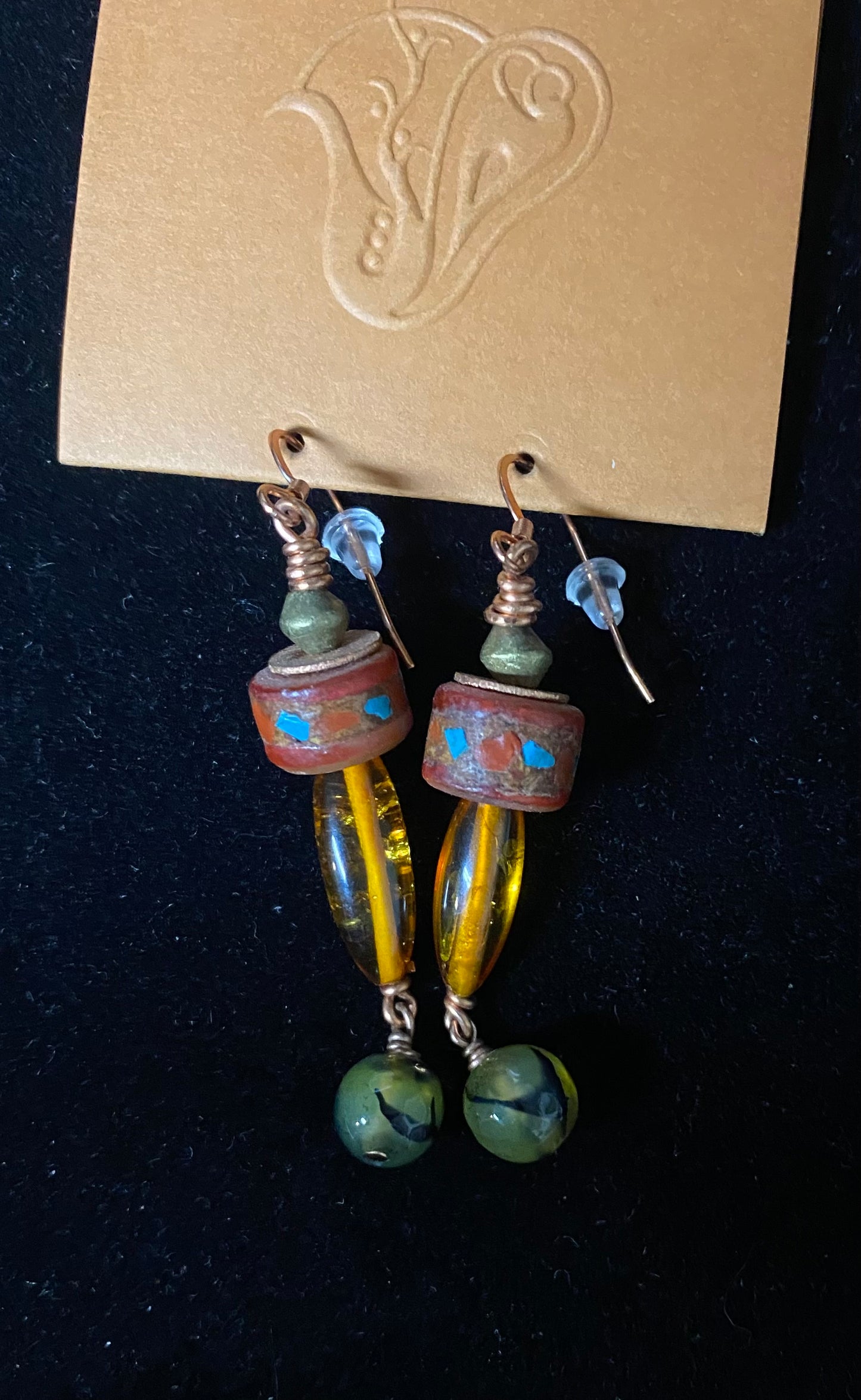 Pair of beaded earrings on a black background with a brand card above.