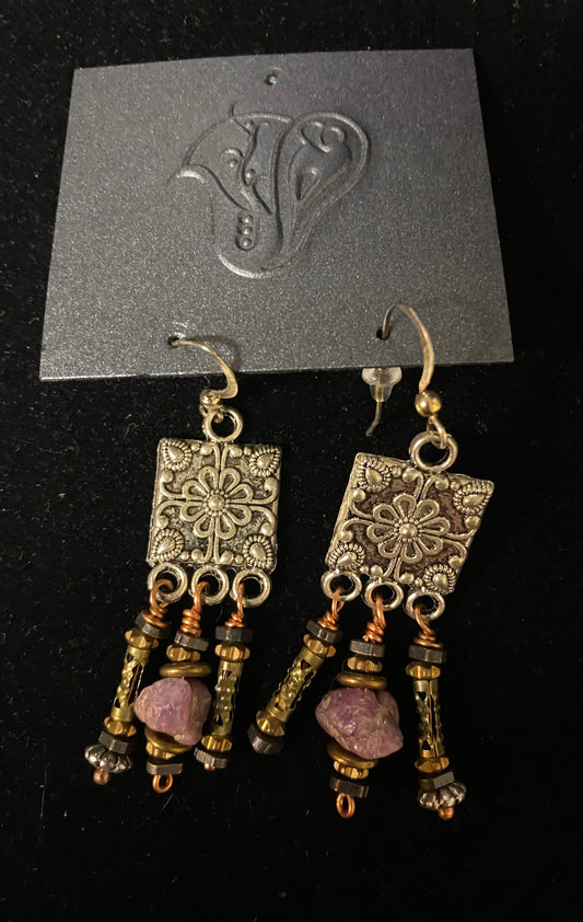 Pair of ornate earrings with purple stones on a black card with a brand logo.