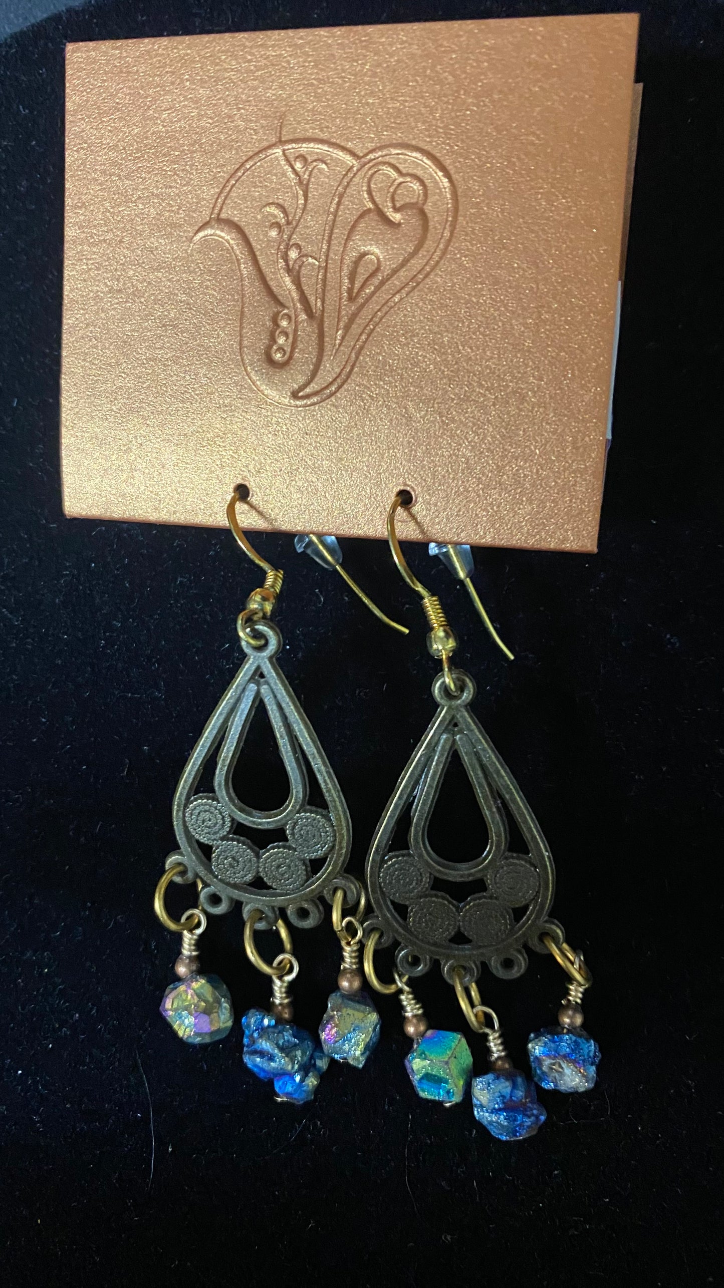 Pair of black teardrop earrings with blue beads on a gold card with a floral design.