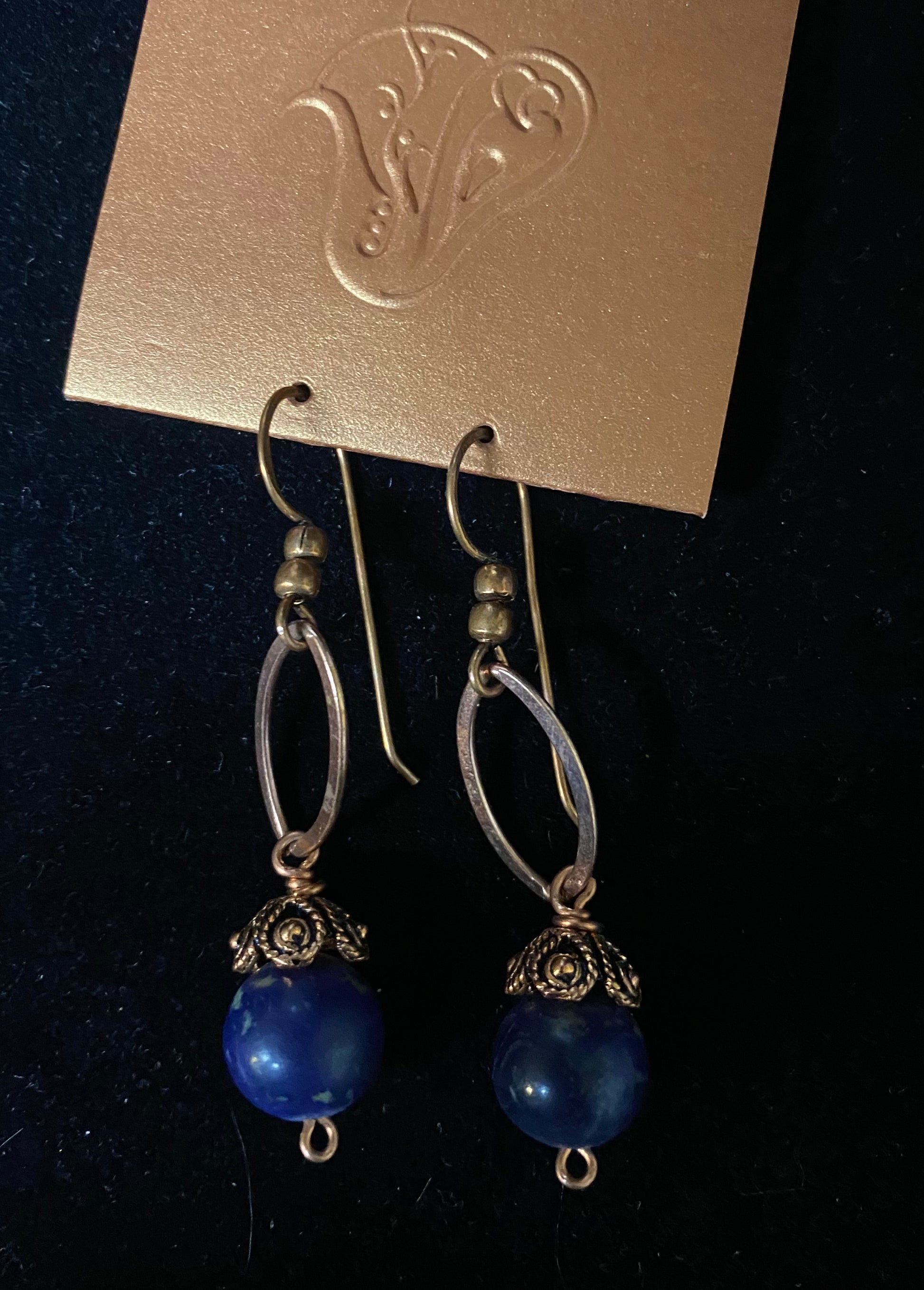 Pair of blue beaded earrings on a dark background with a brand card above.