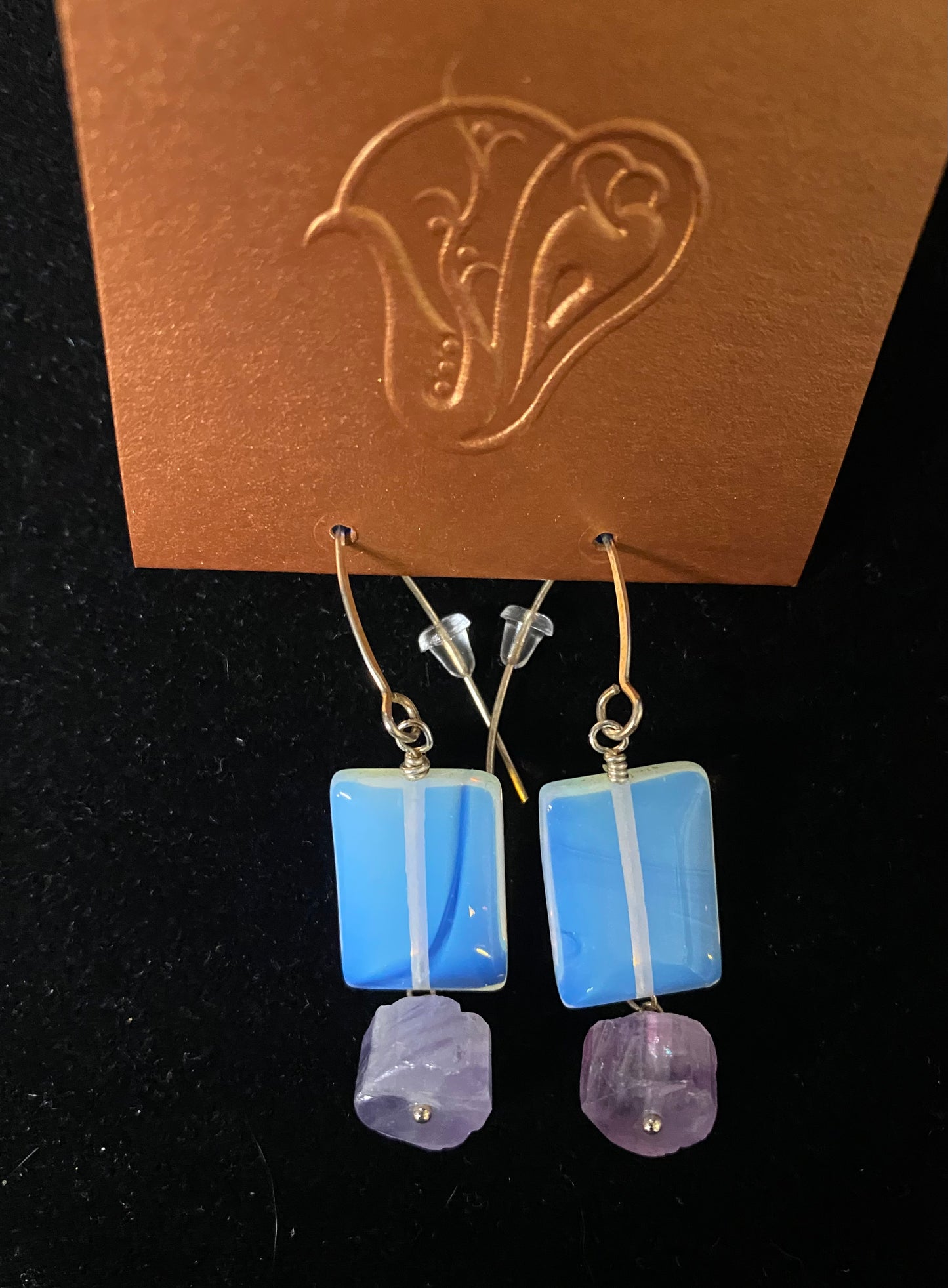 Blue and purple earrings on a brown card with floral design