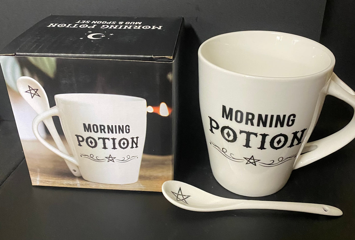 White mug with 'Morning Potion' text and matching spoon on a black surface, with packaging in the background.