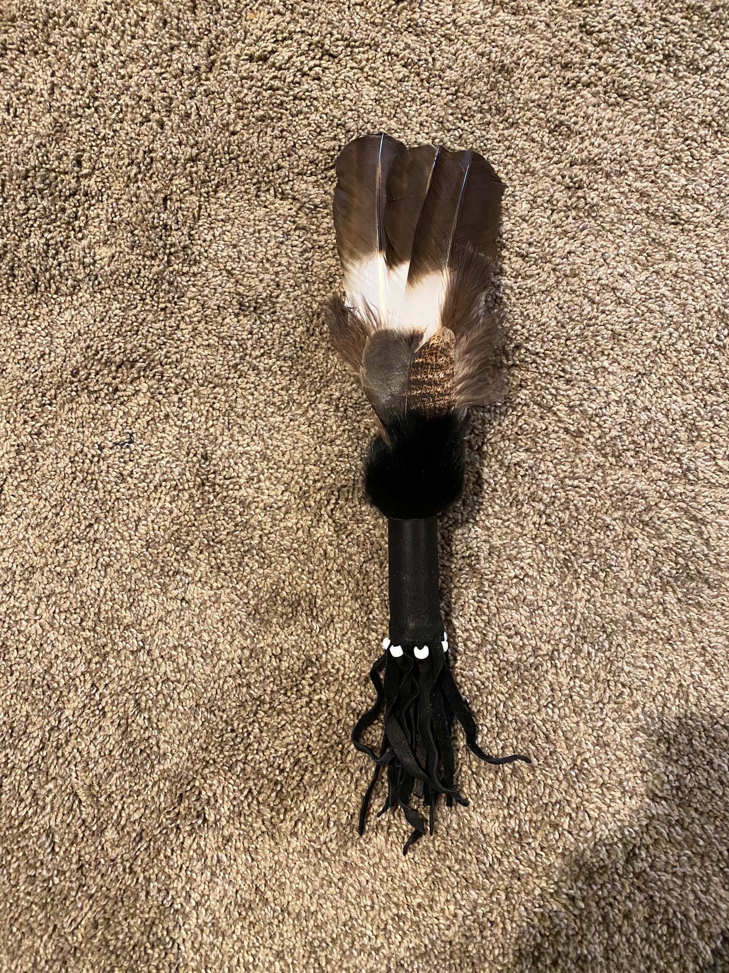 Black feather duster with feathers on a beige carpet