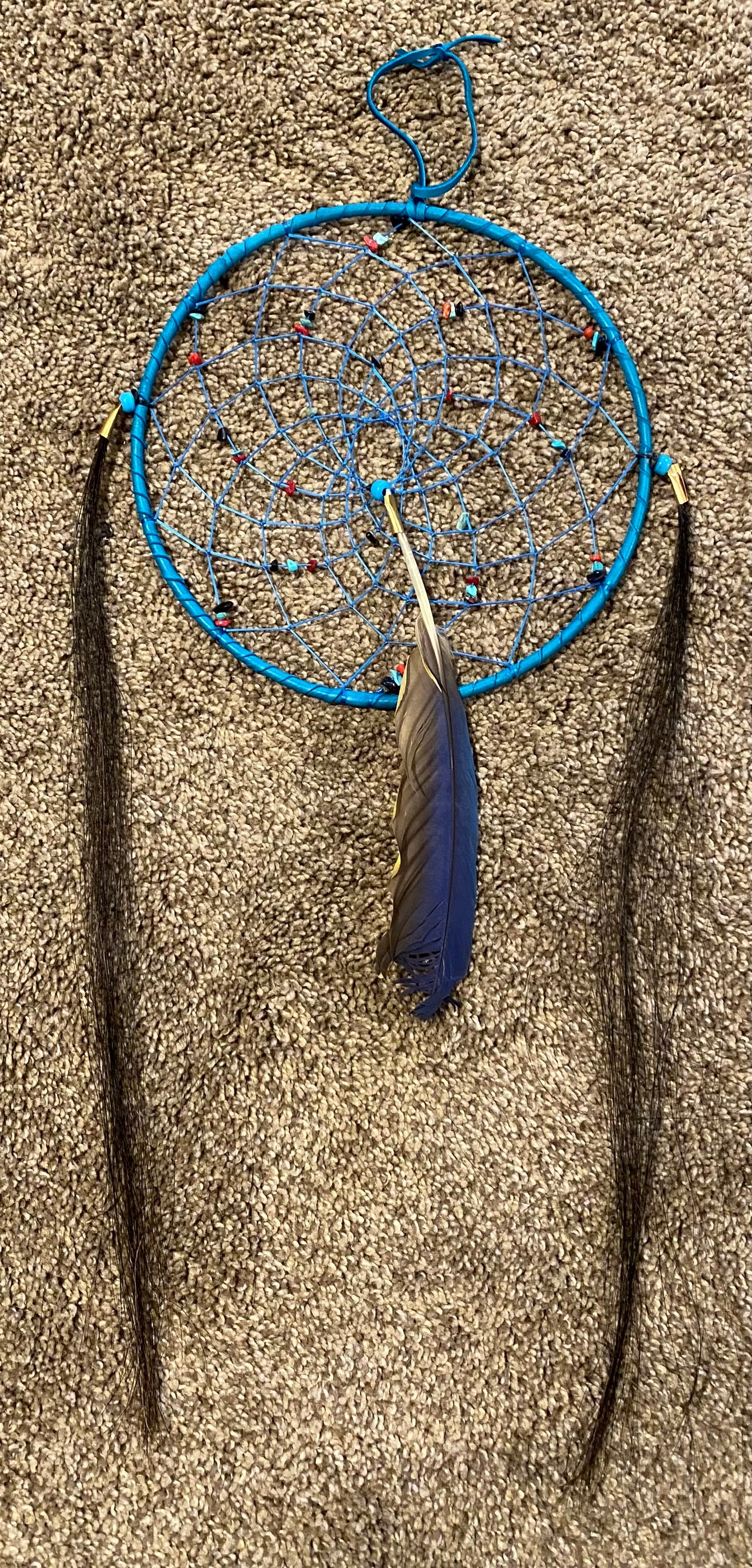 Dreamcatcher with blue web and feathers on a sandy background