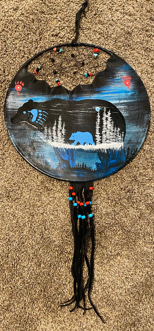 Decorative wall hanging with bear silhouette, trees, and beaded details on a textured surface.