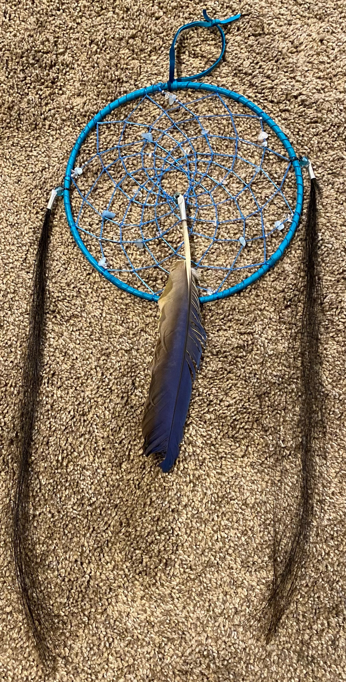 Blue dreamcatcher with feathers on a sandy background