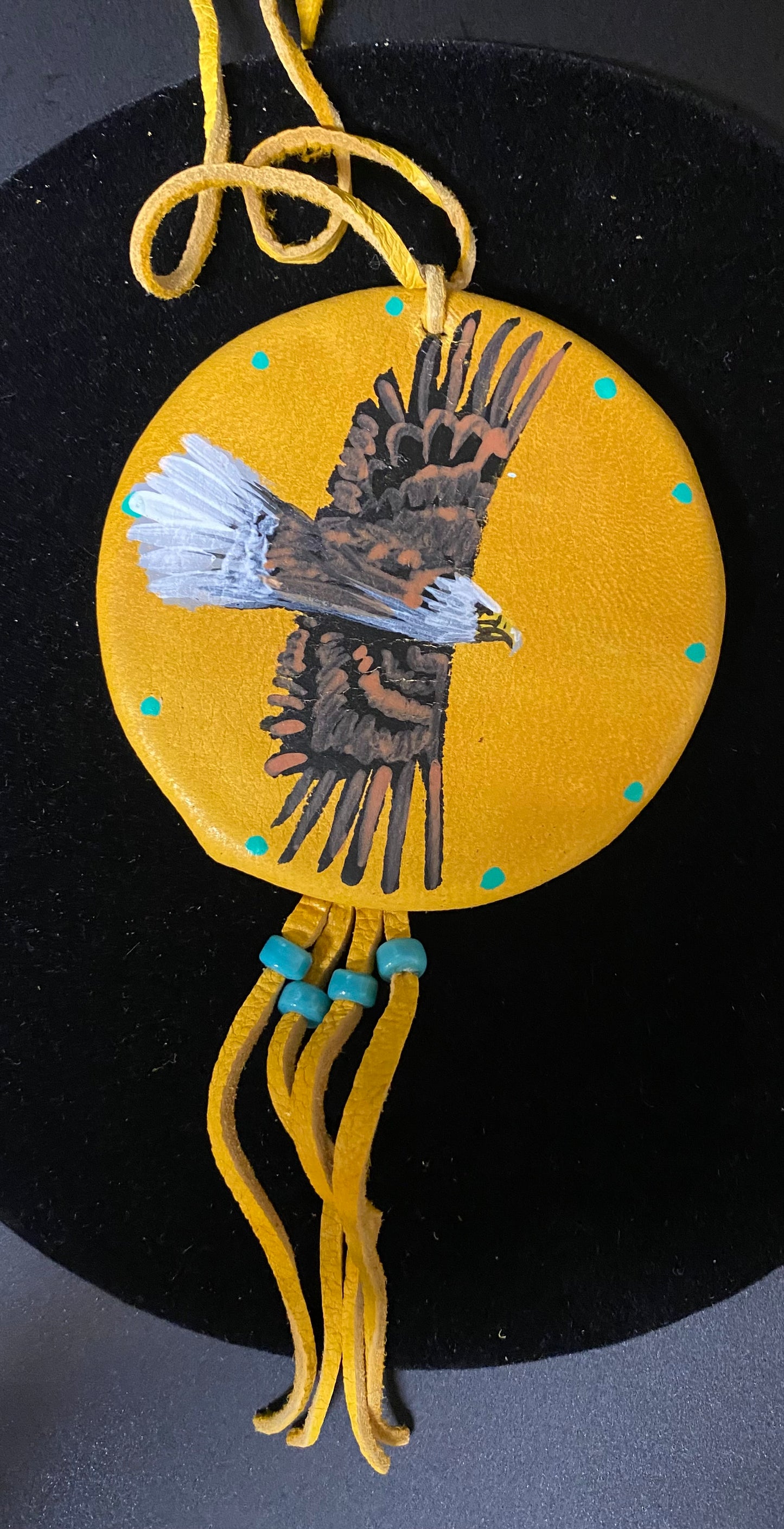 Decorative item with an eagle design on a yellow circle, hanging from a yellow string against a black background.