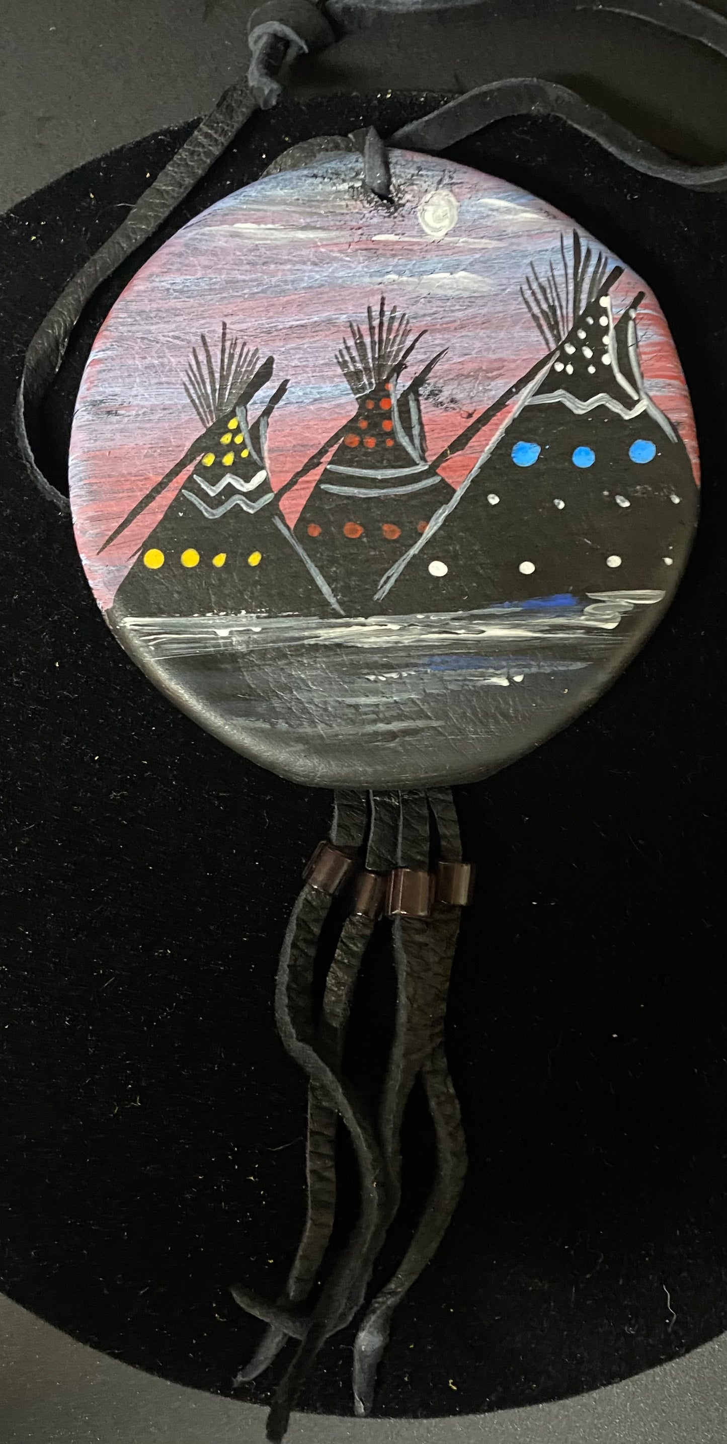 Decorative bolo tie with painted design of teepees on a dark background