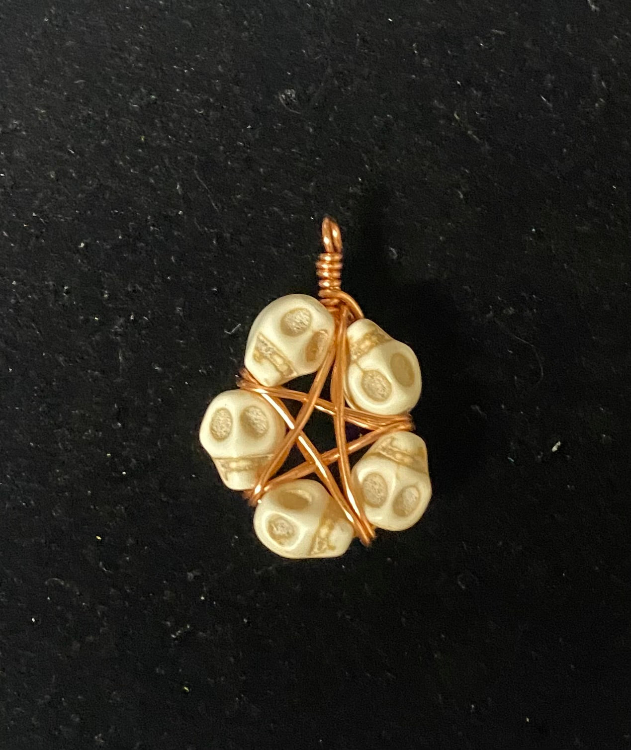 Skull-shaped pendant Howlite with copper wire wrapping on a black background