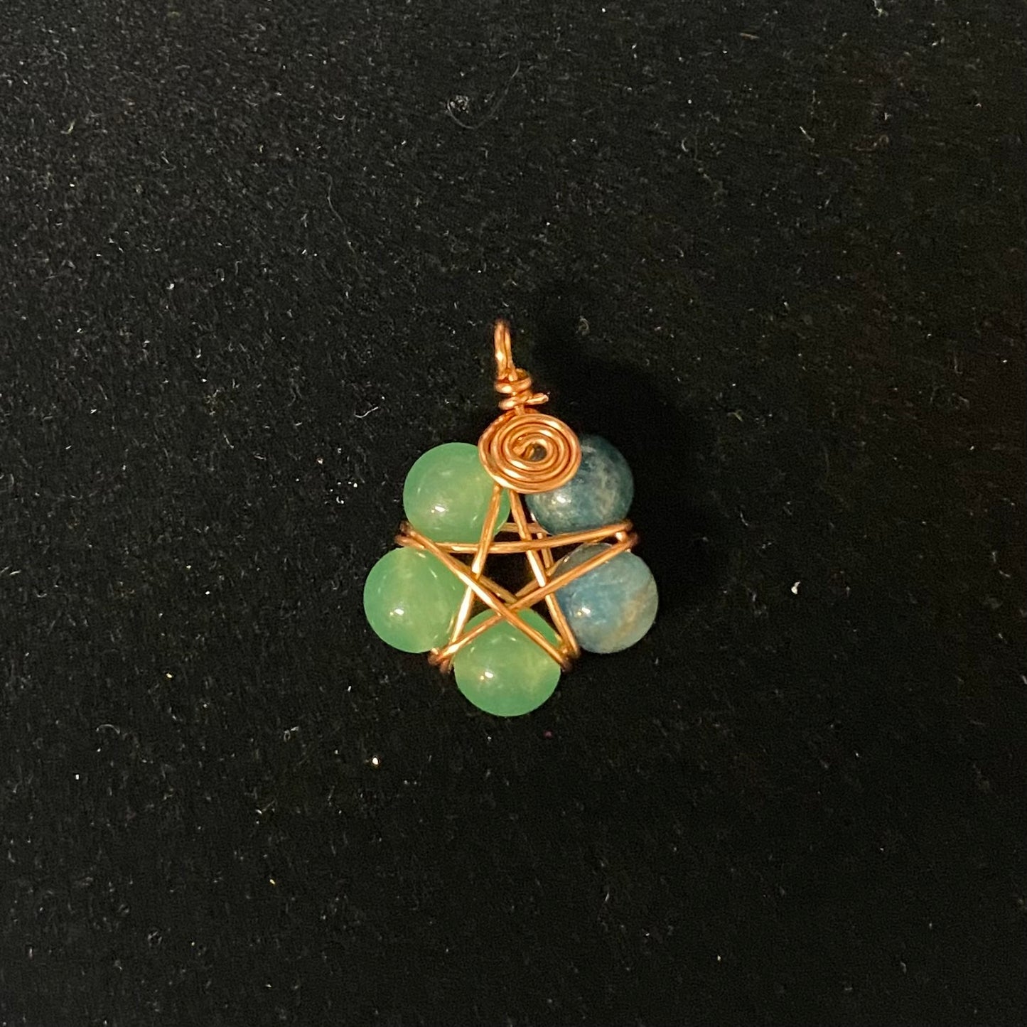 Jewelry pendant with green beads and copper wire wrapping on a black background